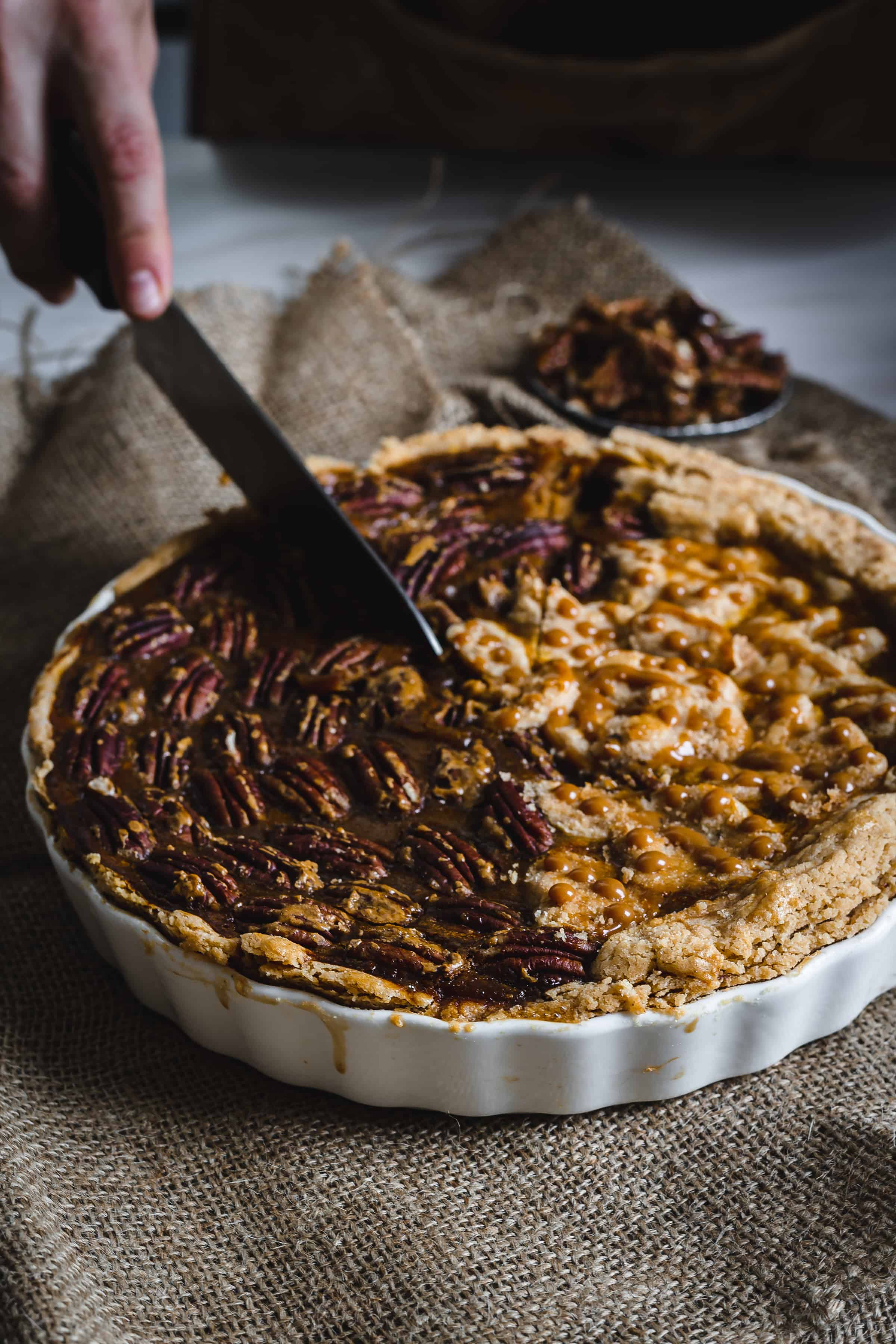 hands cutting baked pumpkin pecan pie