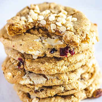 stack of cookies with top cookie with chew taken out  Apple olive oil cake White chocolate cookies with cranberries and pistachios THUMBNAIL 360x360
