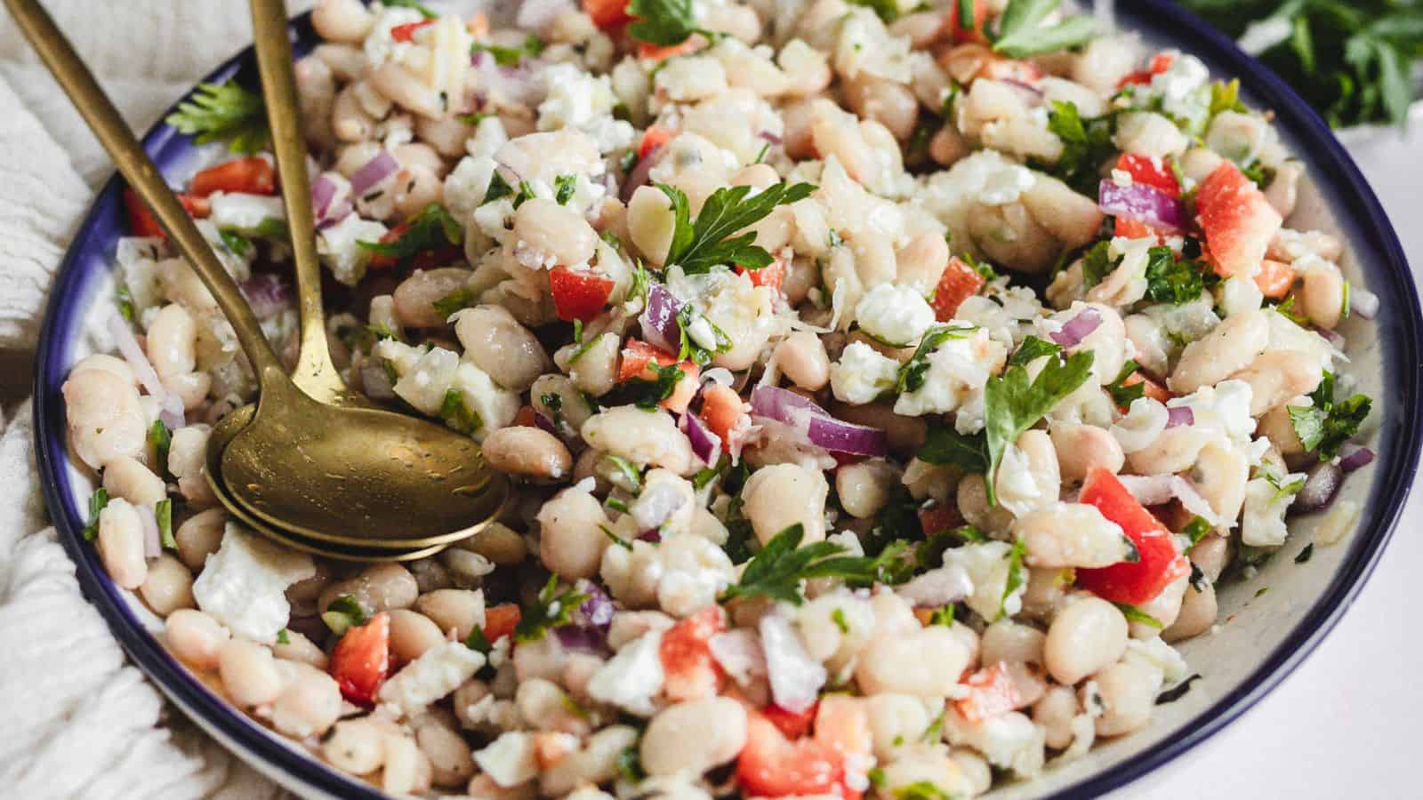 Side view of white bean salad in bowl with tongs.