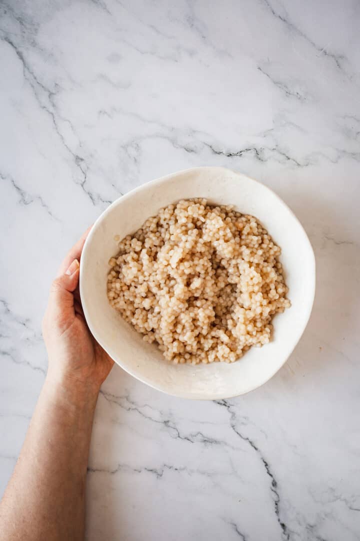 hand serving pearl couscous in bowl