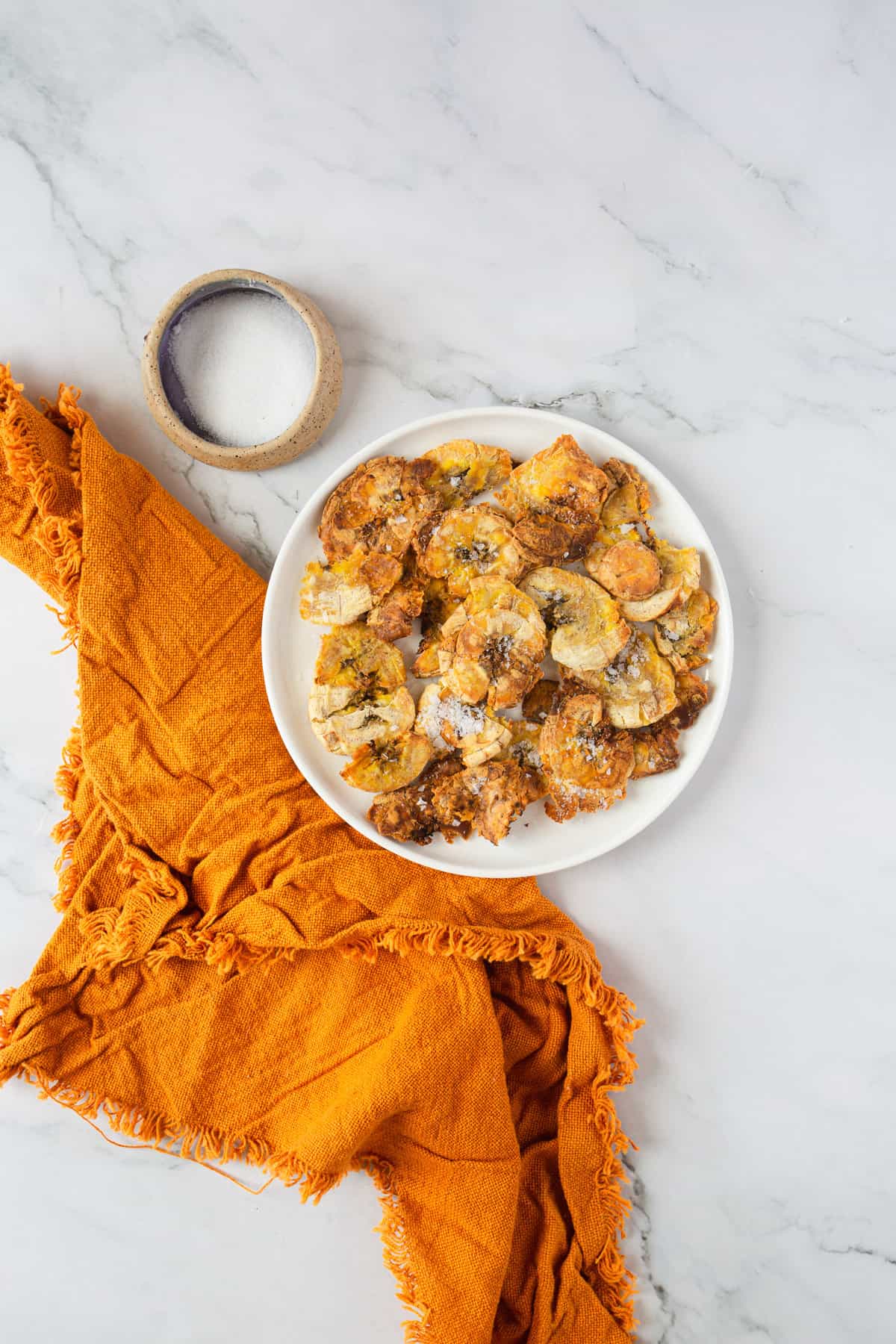 air fryer plantain tostones on white plate with orange napkin