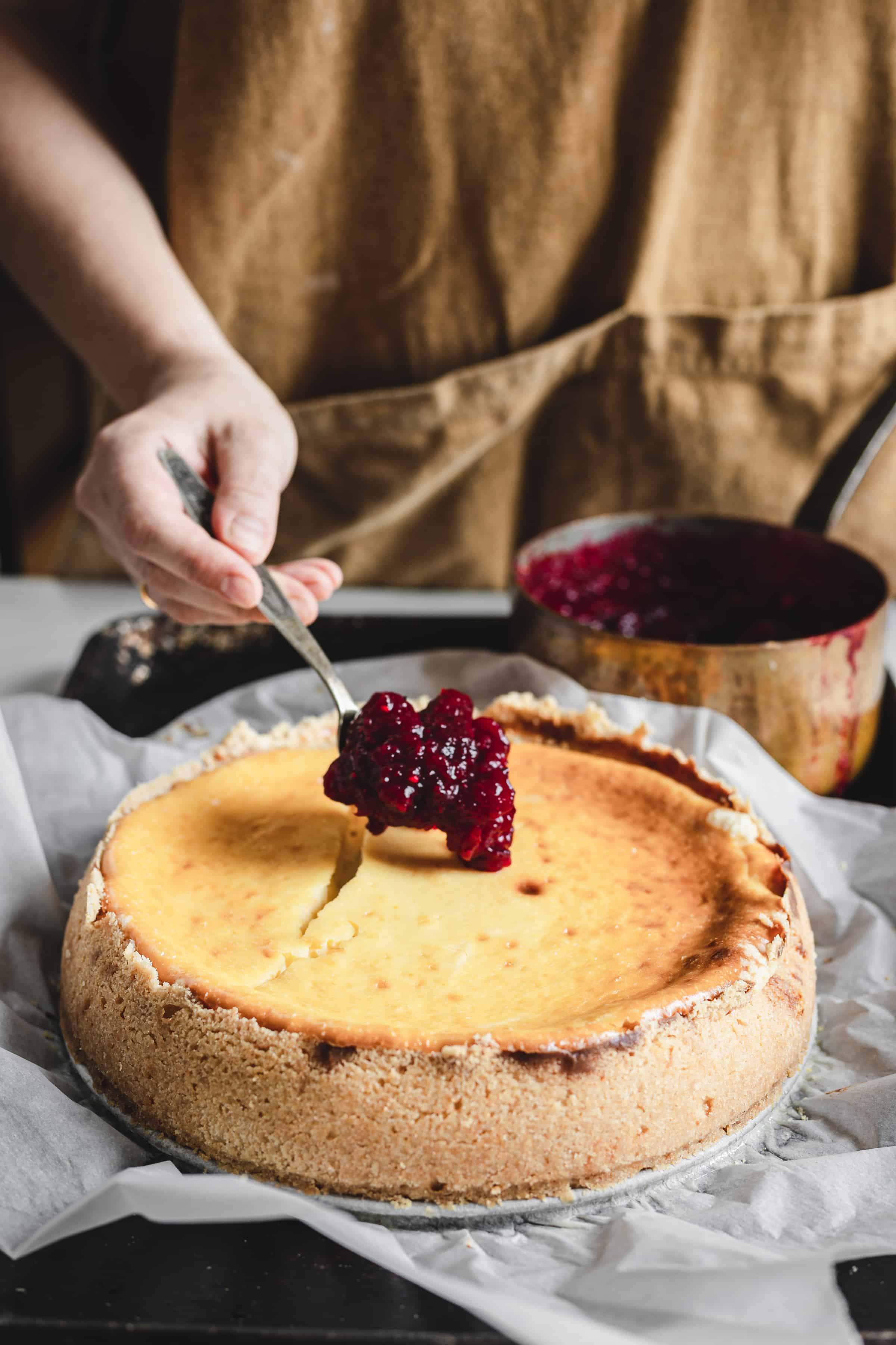 spooning the cranberry topping onto the cheesecake