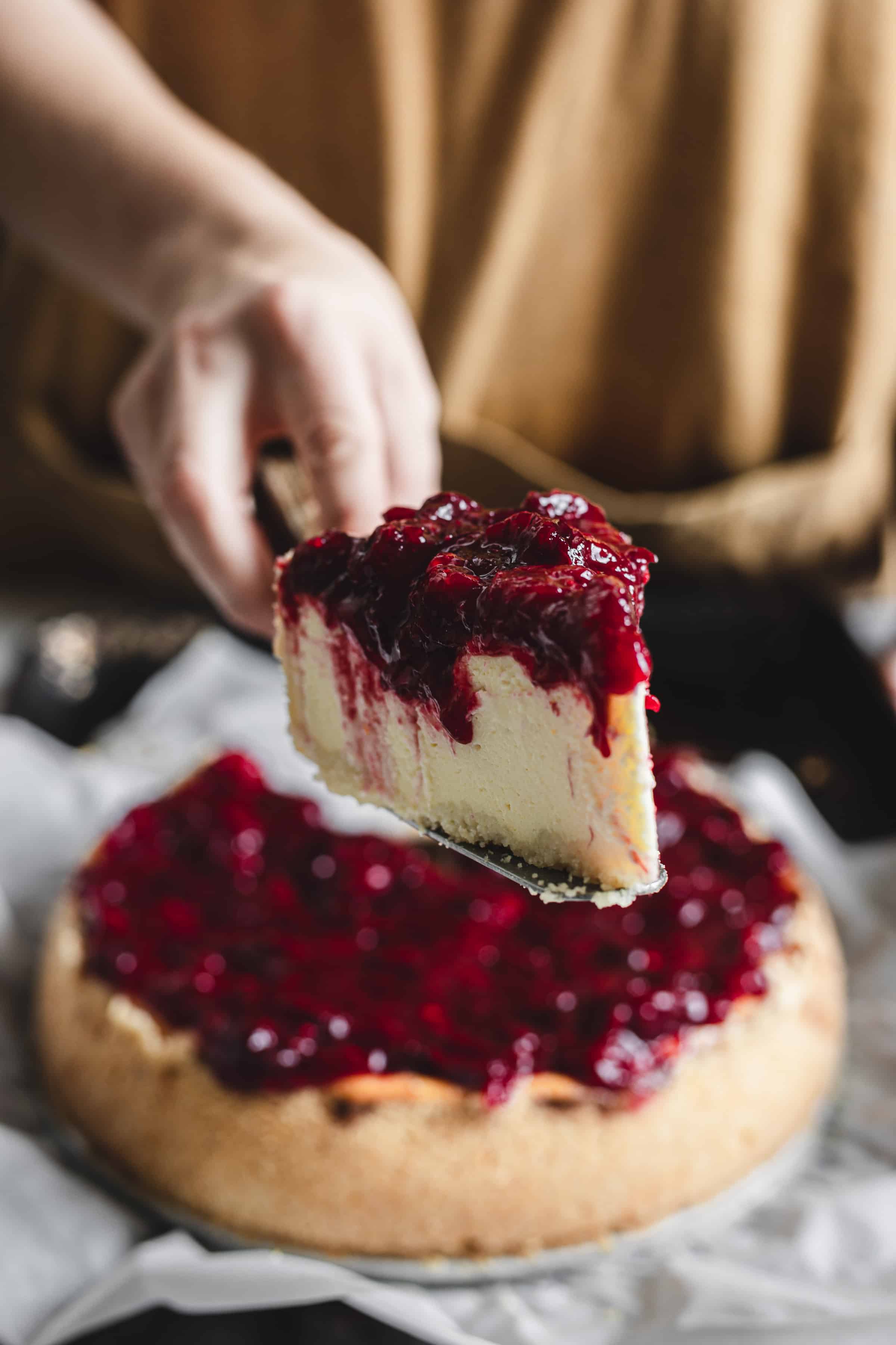 pulling a slice of cheesecake with cranberry topping drizzling down the sides