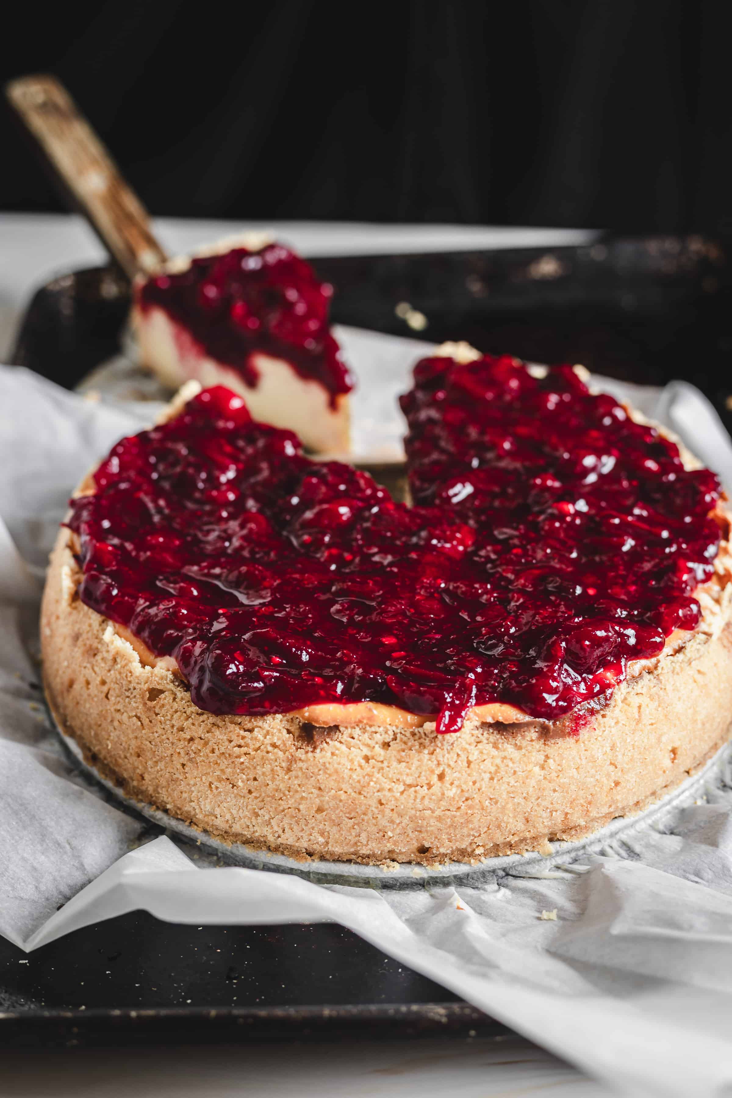 pulling a slice of cheesecake with cranberry topping drizzling down the sides