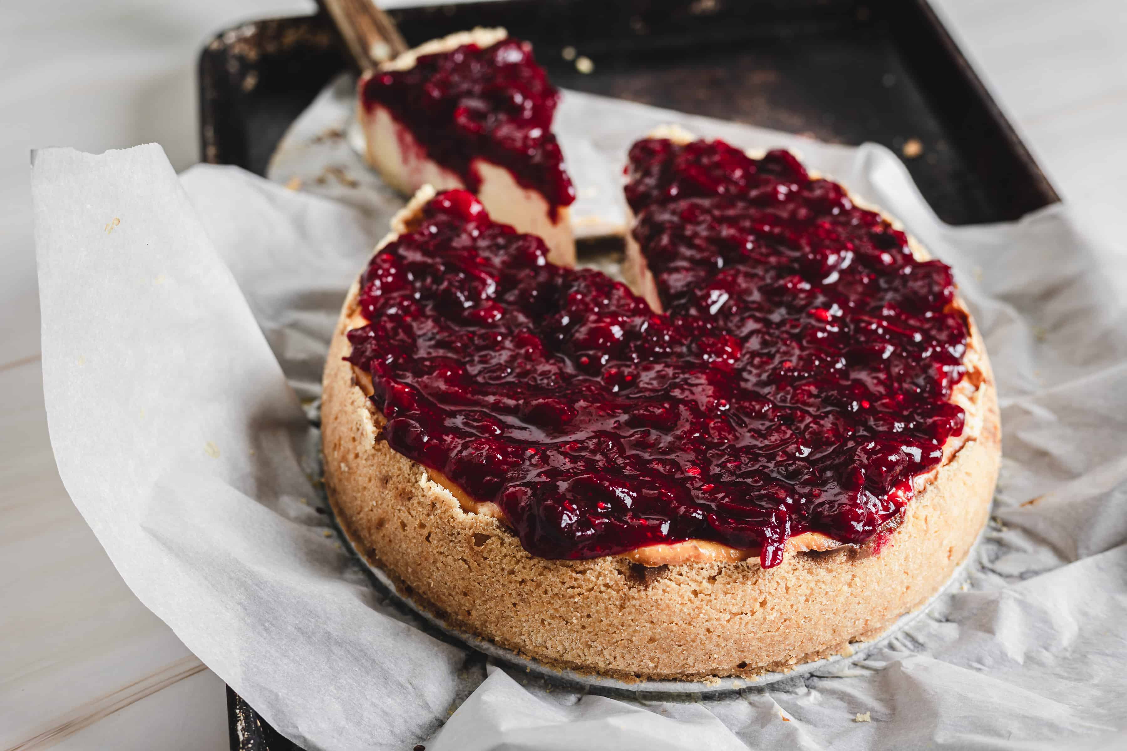 pulling a slice of cheesecake with cranberry topping drizzling down the sides