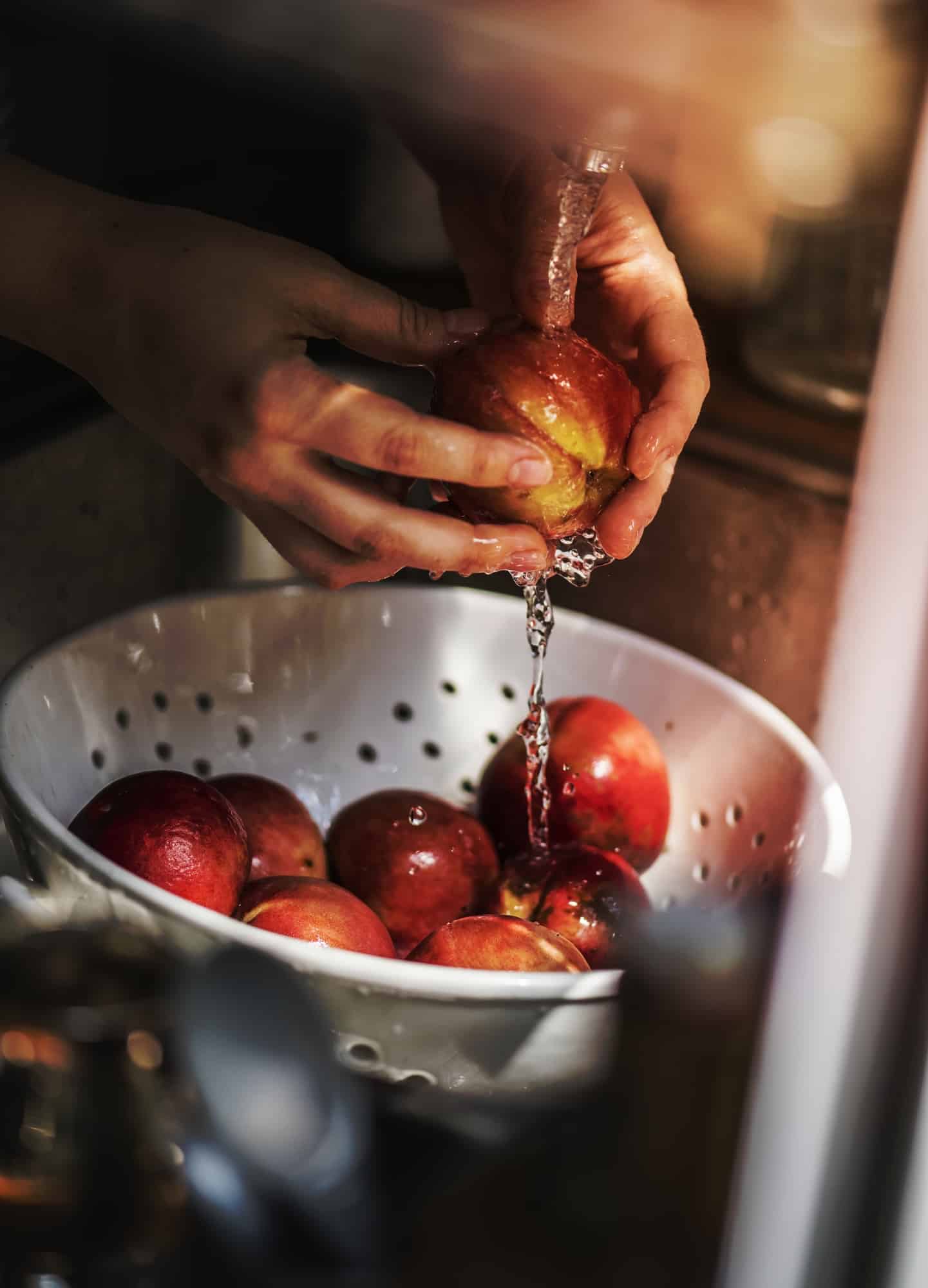 A person washing apples under running water.