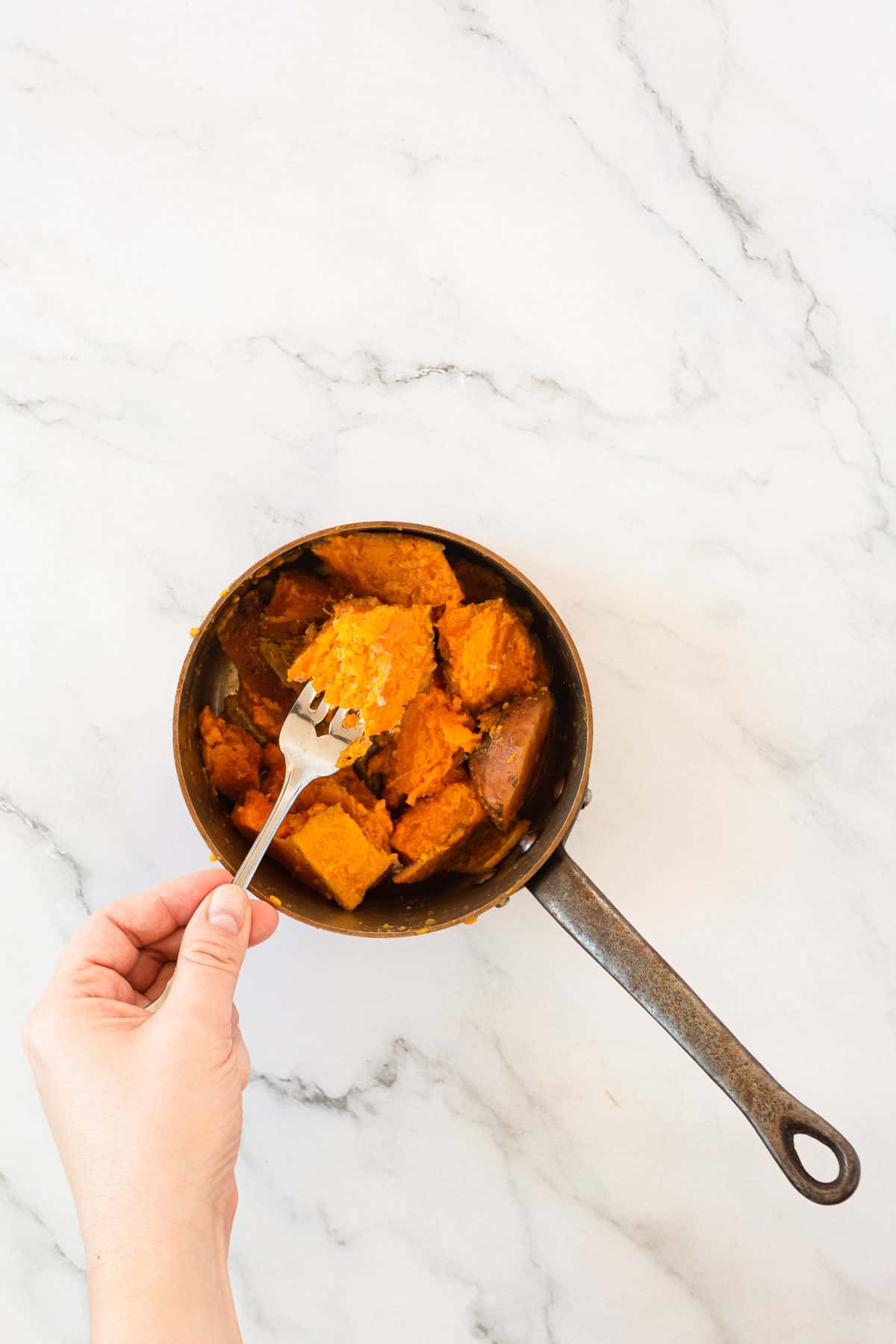 Boiled sweet potatoes in a small sauce pan with a fork.