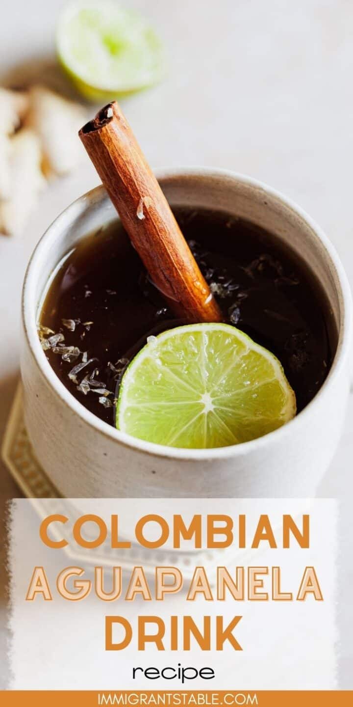 A white mug of aguapanela garnished with a cinnamon stick and lime slice.