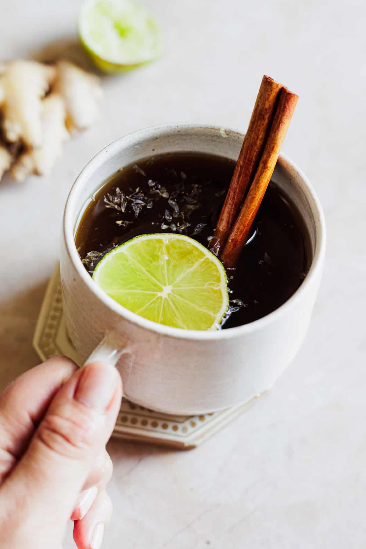 A white mug of aguapanela garnished with a cinnamon stick and lime slice.