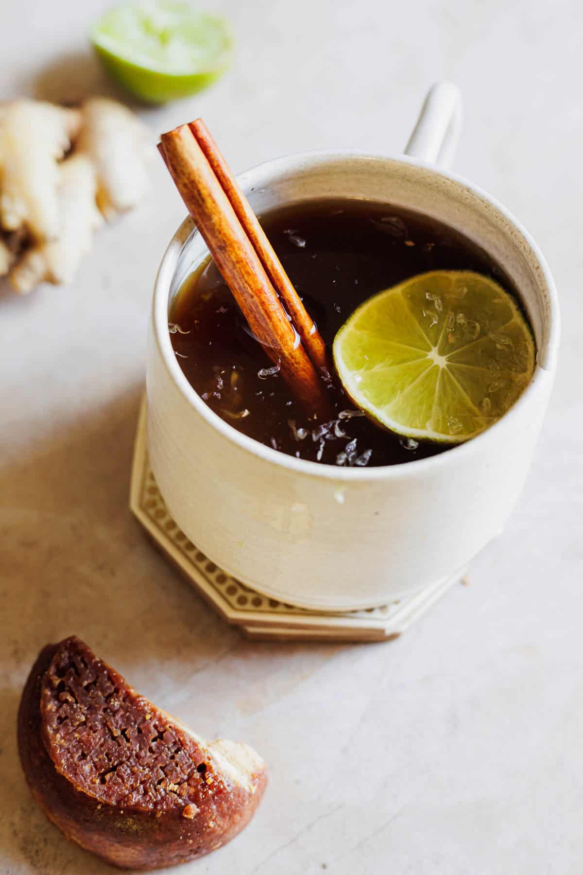 A white mug of aguapanela garnished with a cinnamon stick and lime slice.