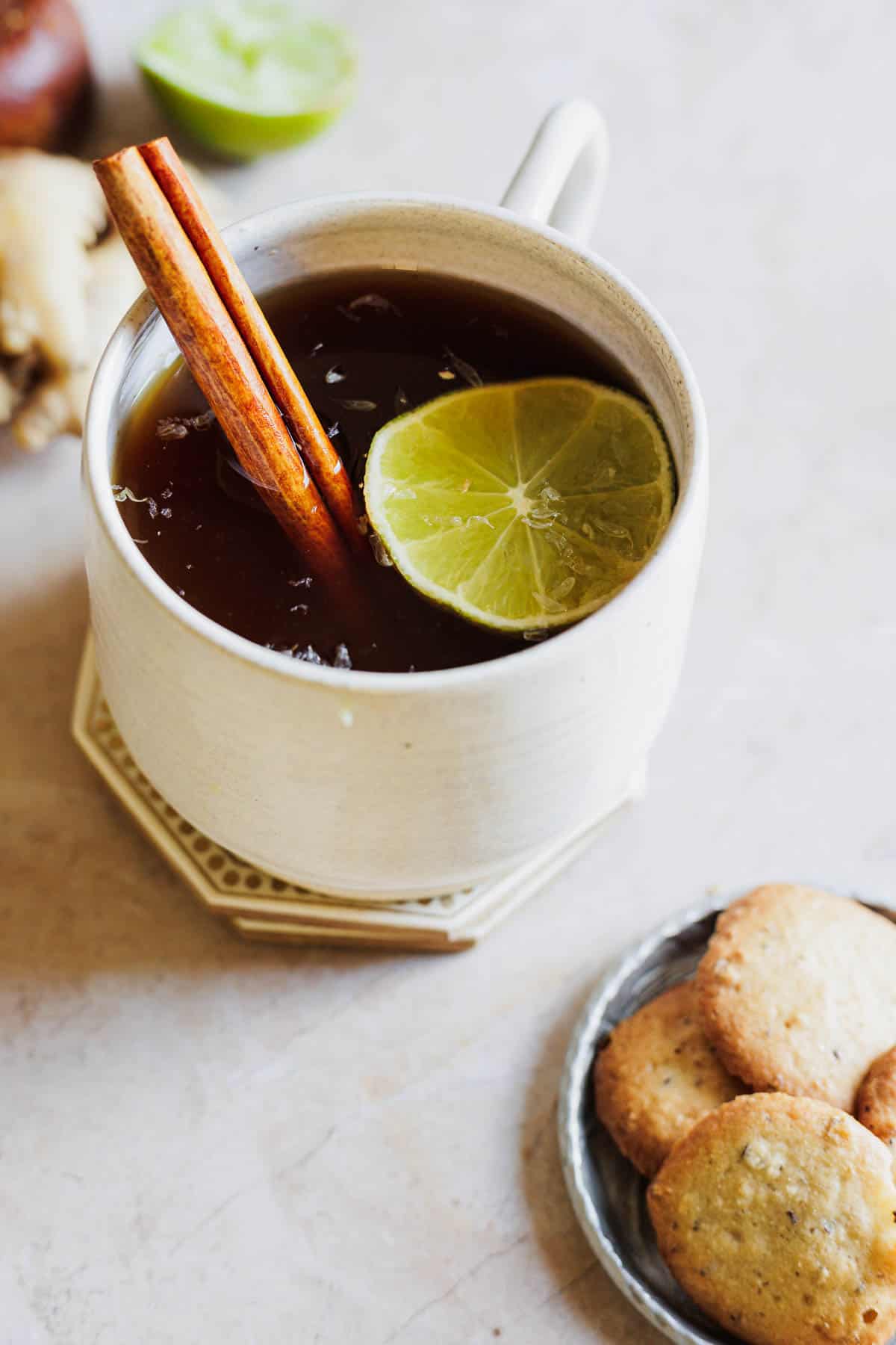 A white mug of aguapanela garnished with a cinnamon stick and lime slice.