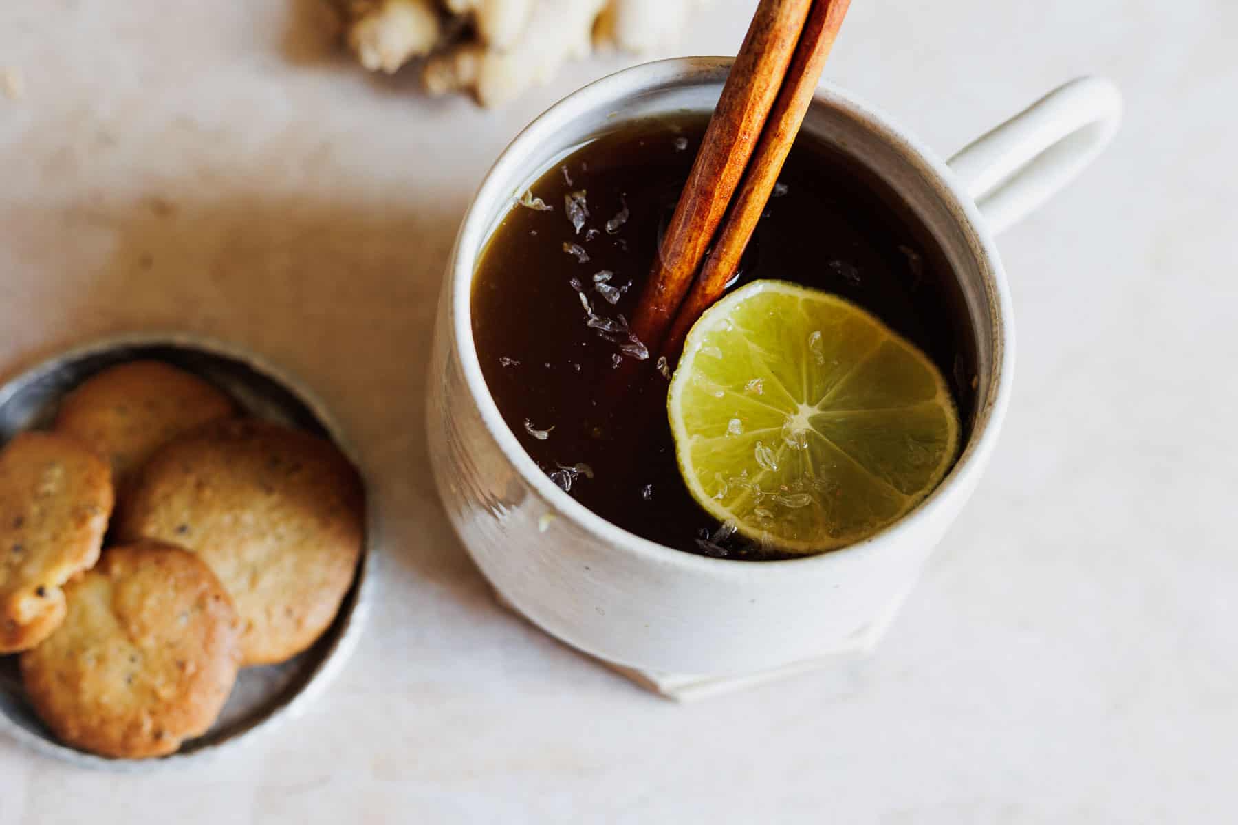 A white mug of aguapanela garnished with a cinnamon stick and lime slice.