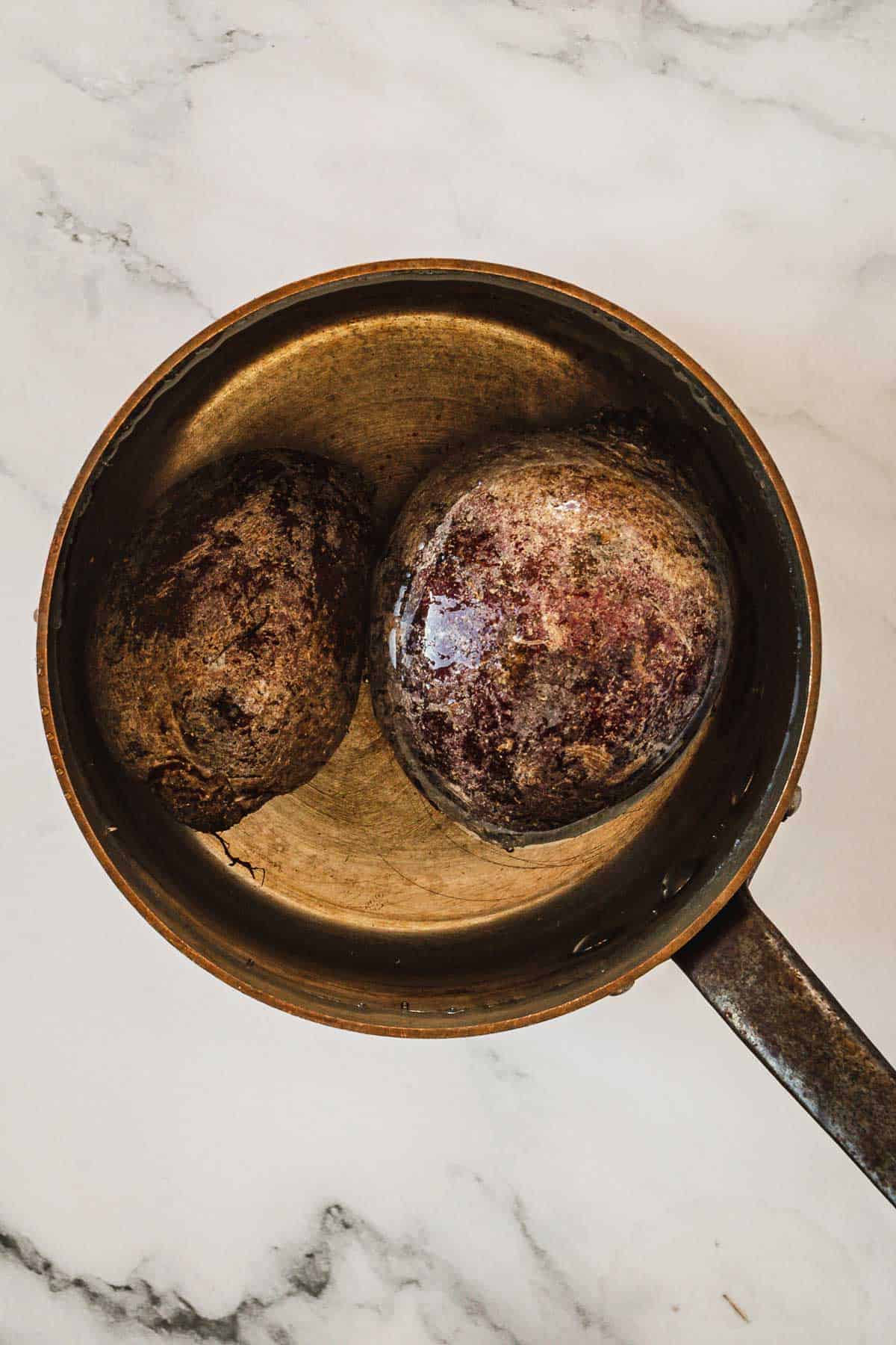 Two whole beets in a saucepan.