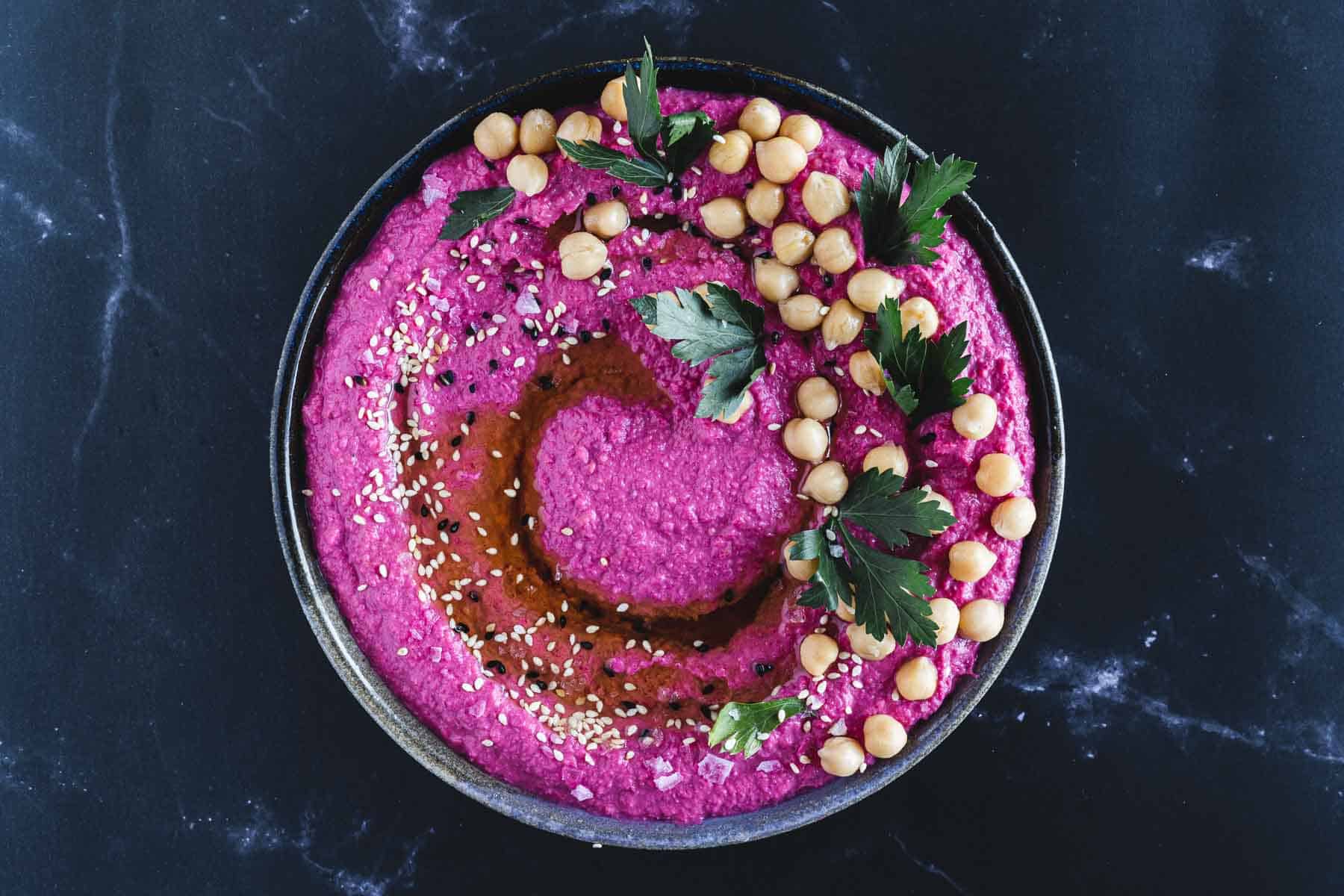 Seasoned and garnished beet hummus in a bowl.