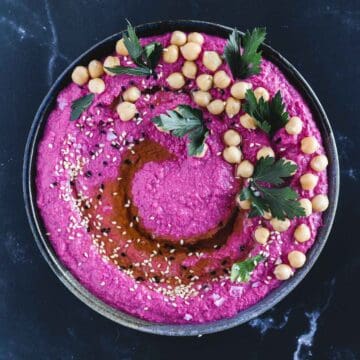 Overhead view of beet hummus with chickpeas, parsley and sesame seeds.