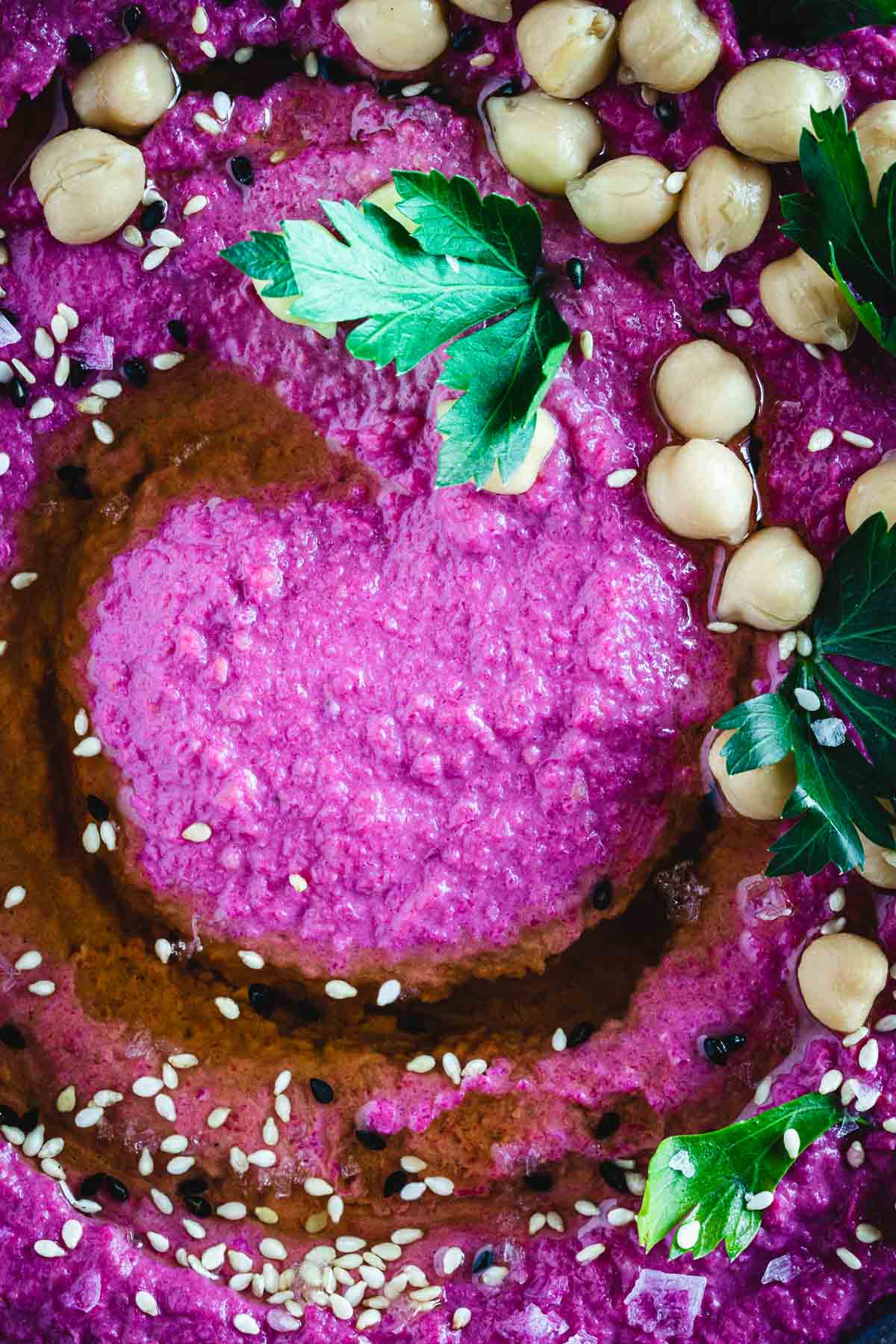 Close up view of beet hummus garnished with chickpeas and sesame seeds.