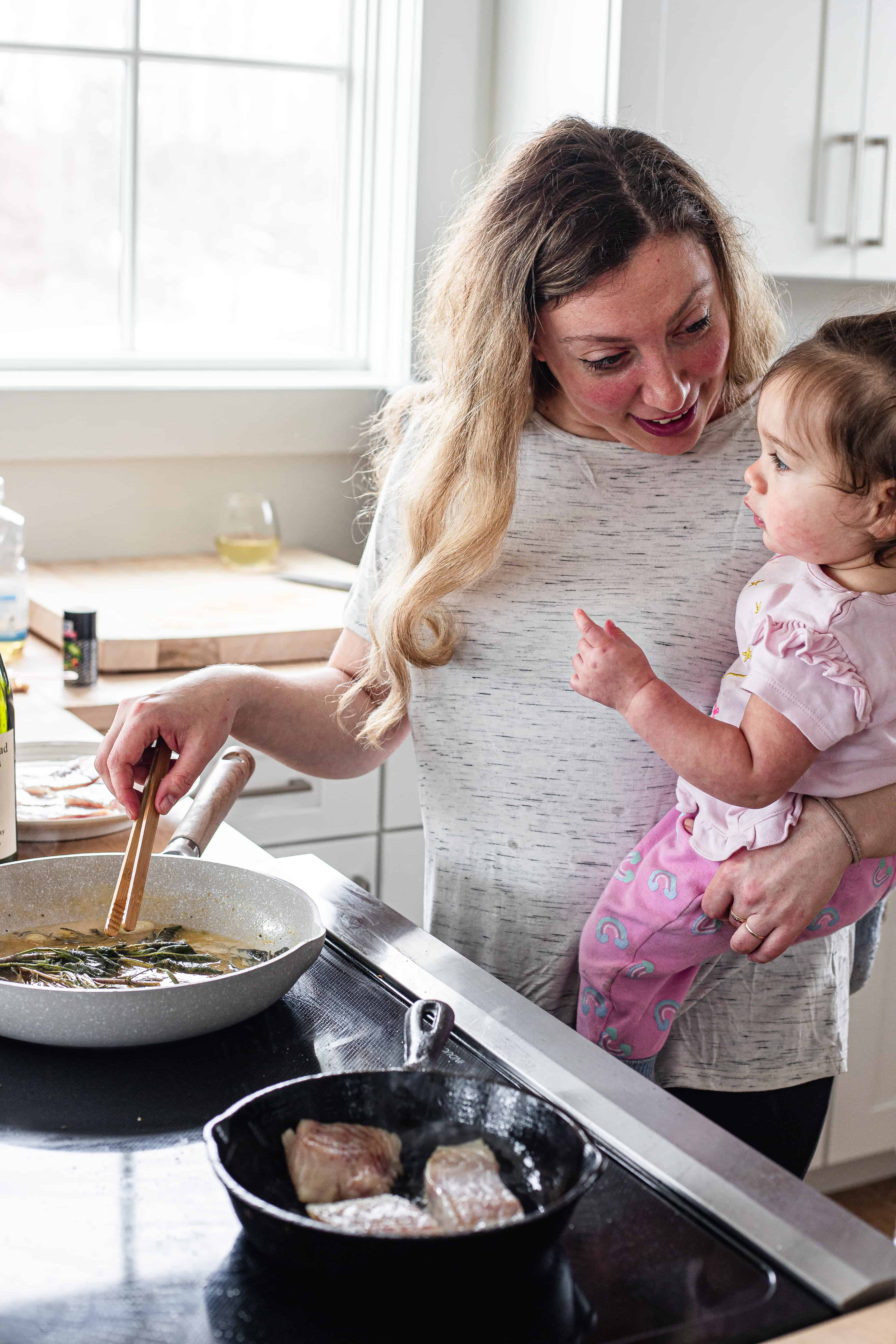 The cook cooking the white wine sauce while holding her baby.