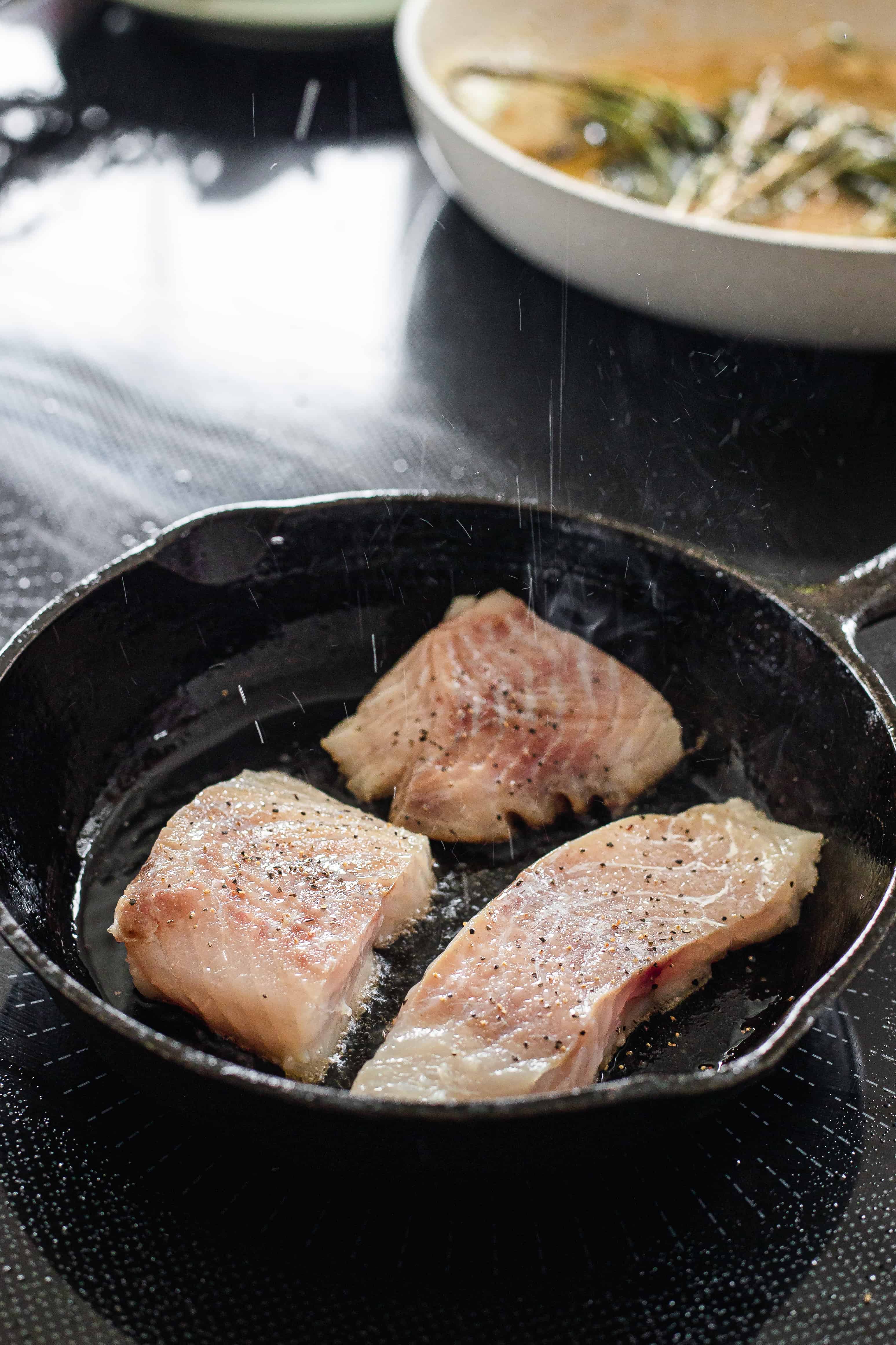 three white fish filets in a skillet.
