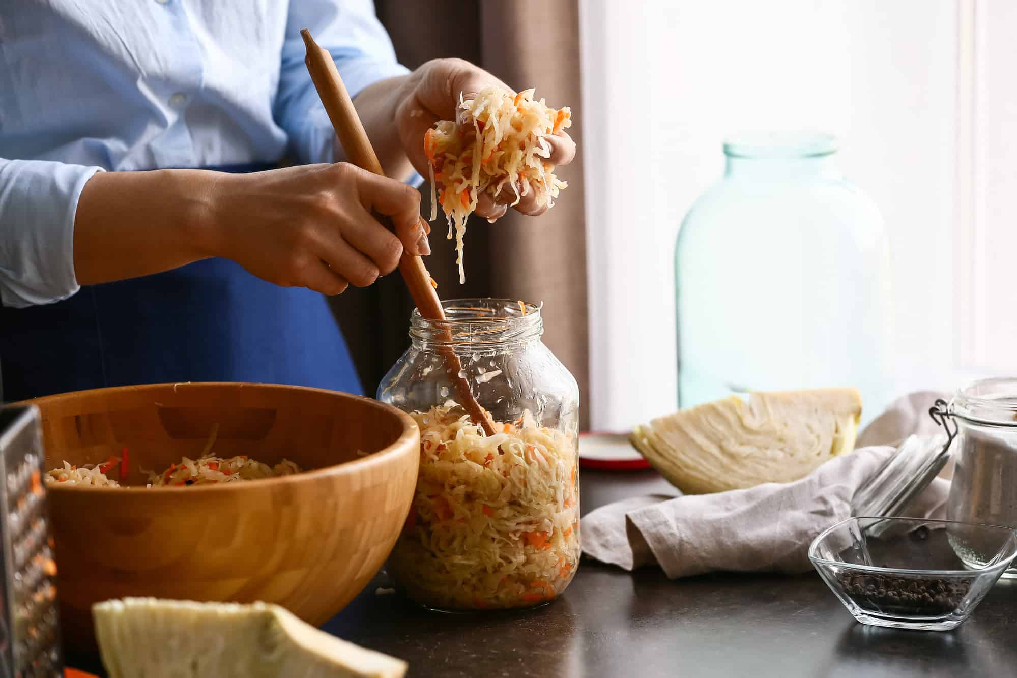 Woman putting tasty sauerkraut into glass jar on table in kitchen, closeup.