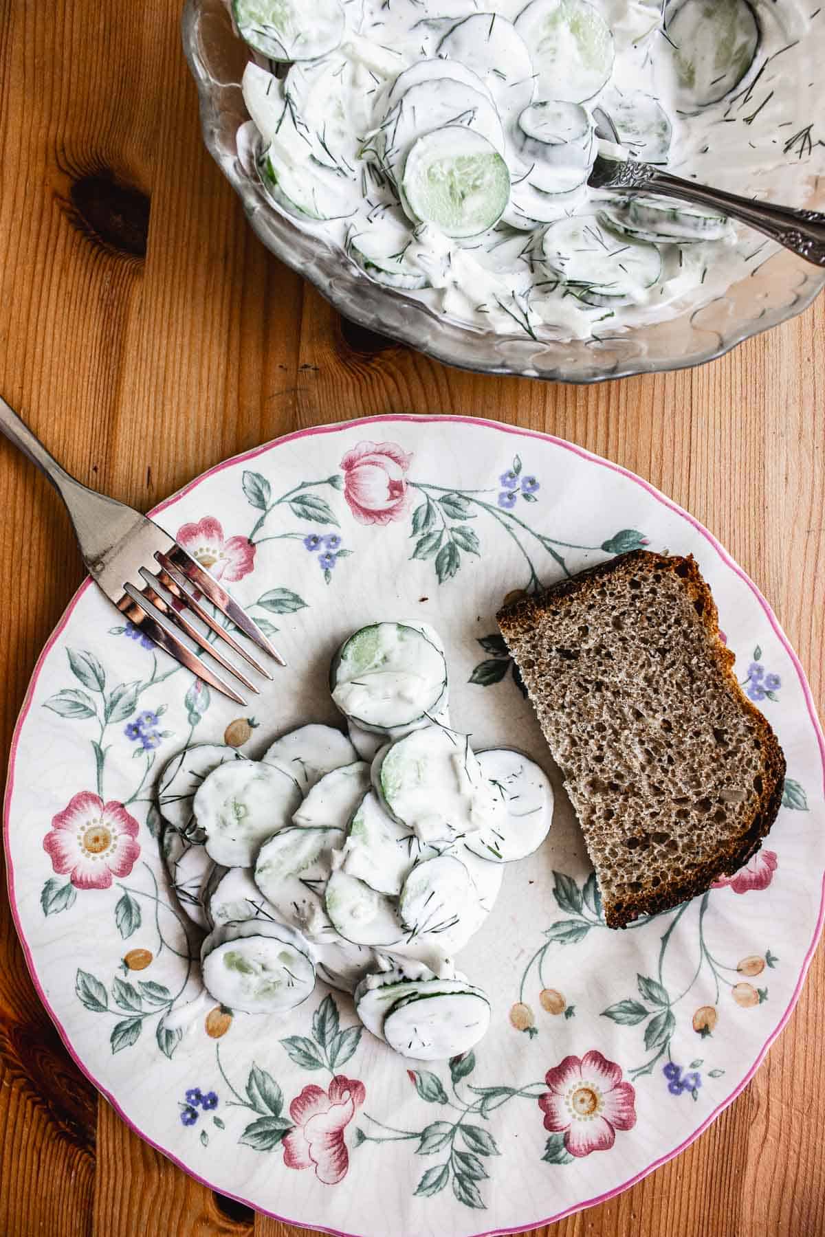 A serving and a bowl of cucumber salad with bread.