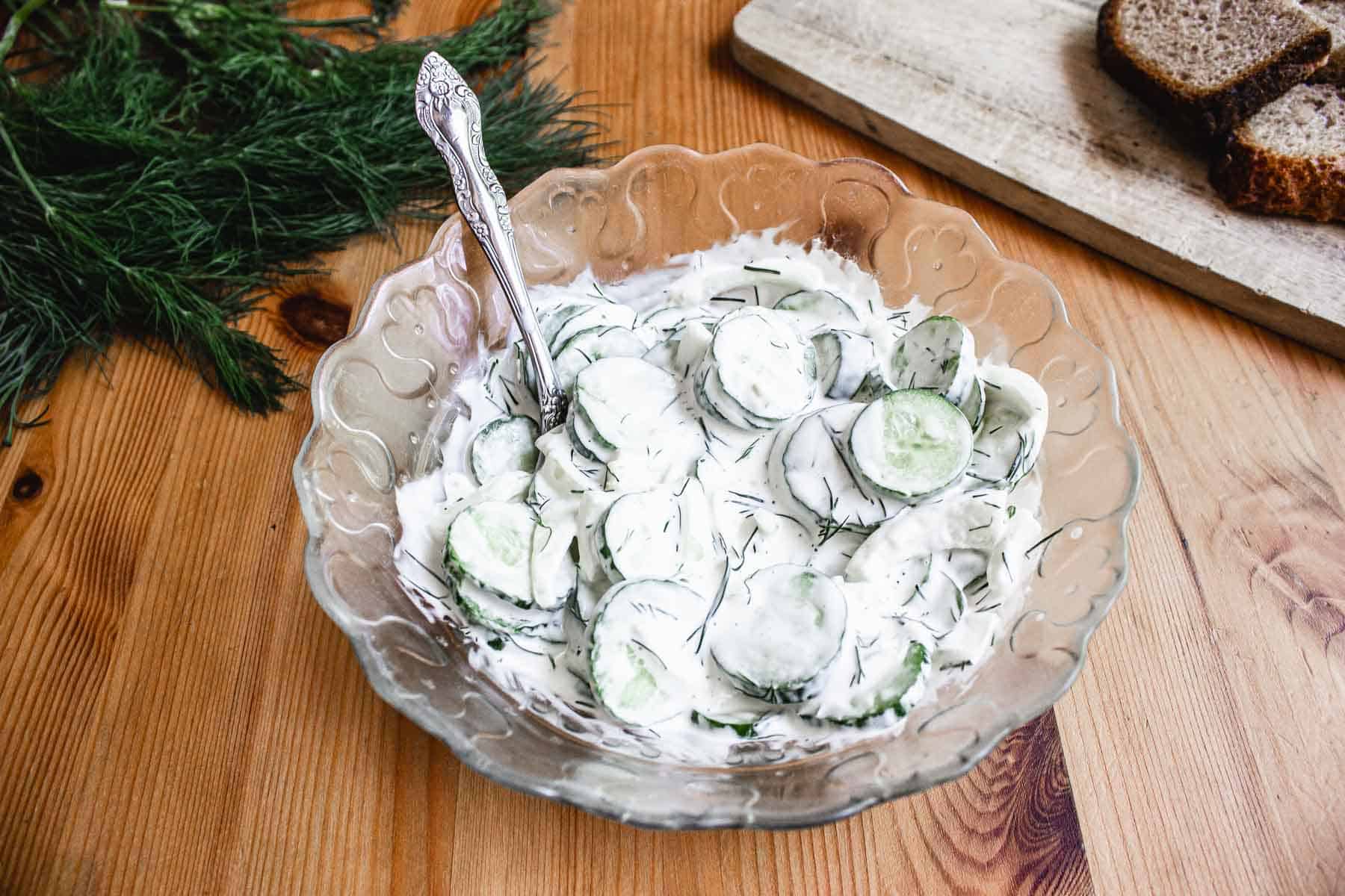 A bowl of cucumber salad with bread and dill.