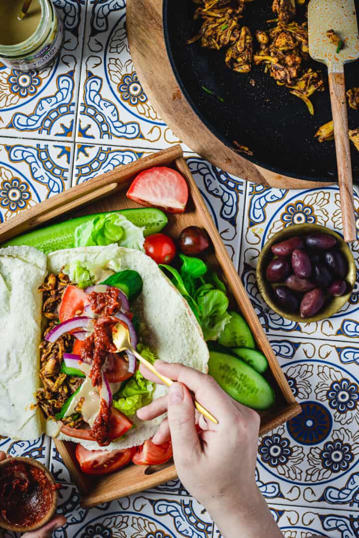 Placing harissa sauce in vegan shawarma pita