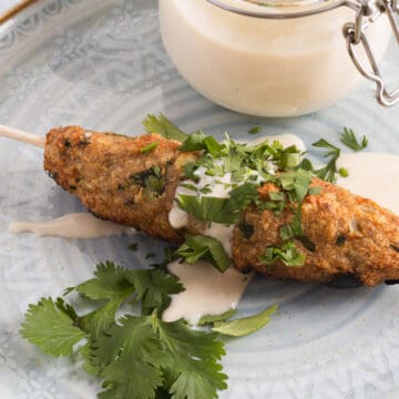 A whole kebab on a skewer on a plate with sauce and cilantro.