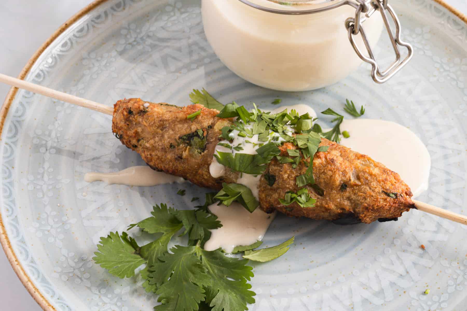 A whole kebab on a skewer on a plate with sauce and cilantro.