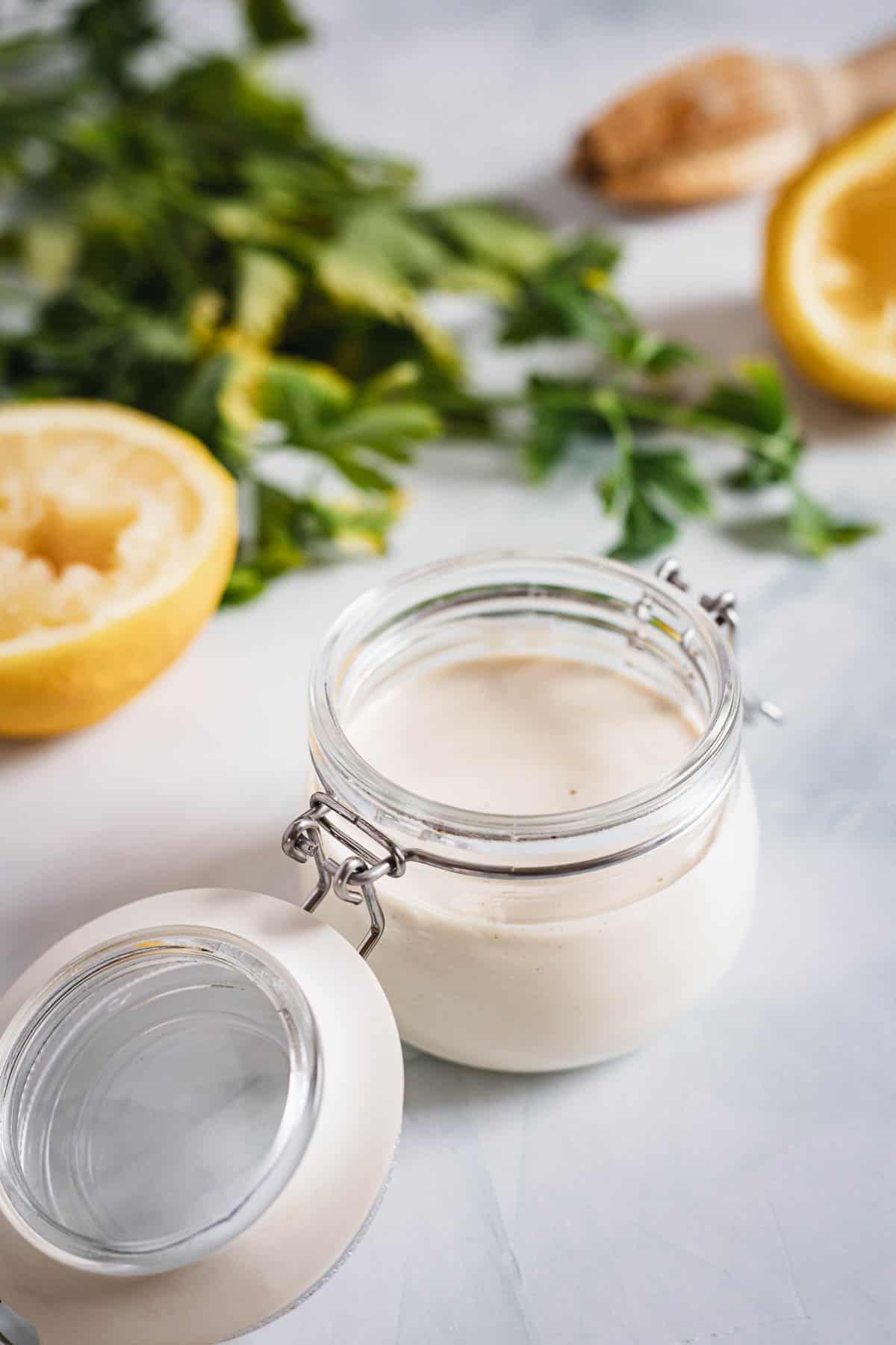 A jar of yogurt with lemons and herbs on a marble table.