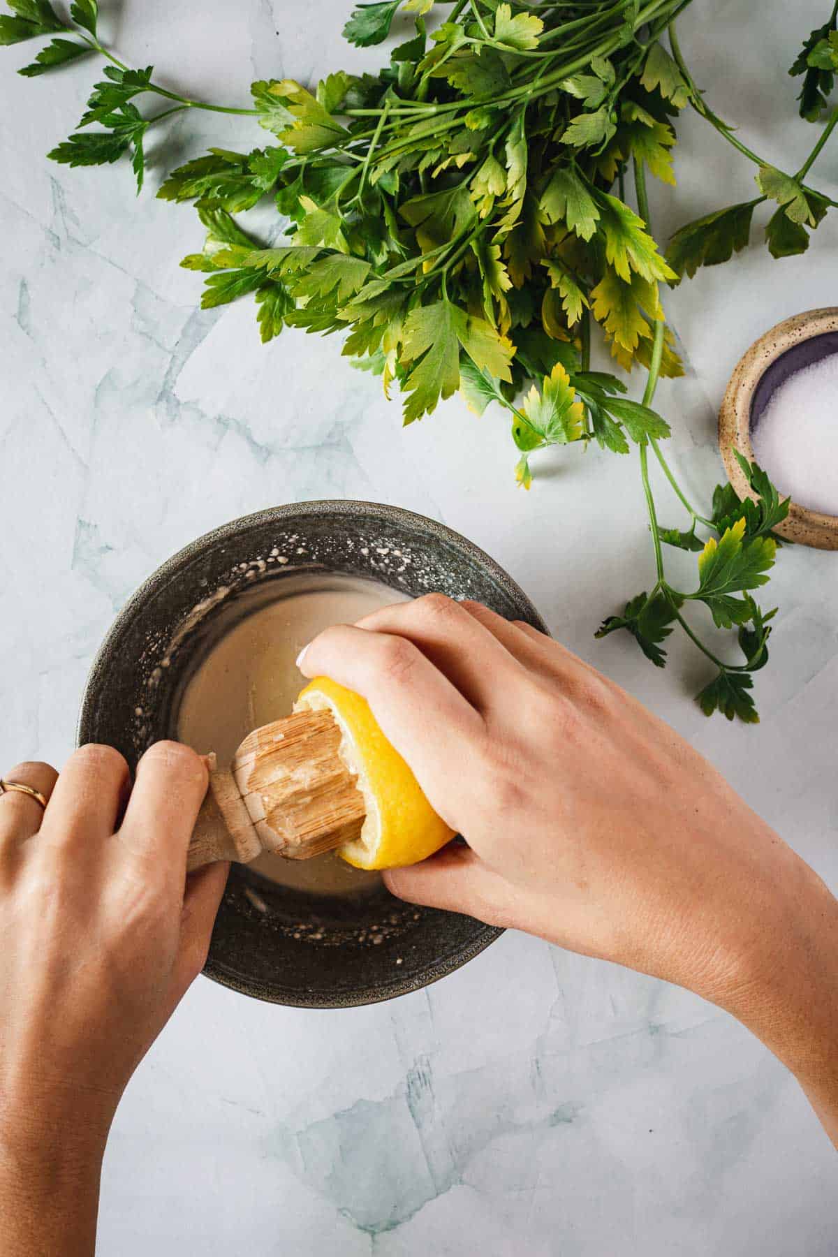 A person squeezing lemon into a bowl of parsley.