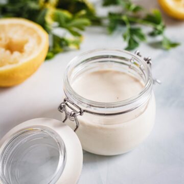 A jar of tahini sauce with parsley.