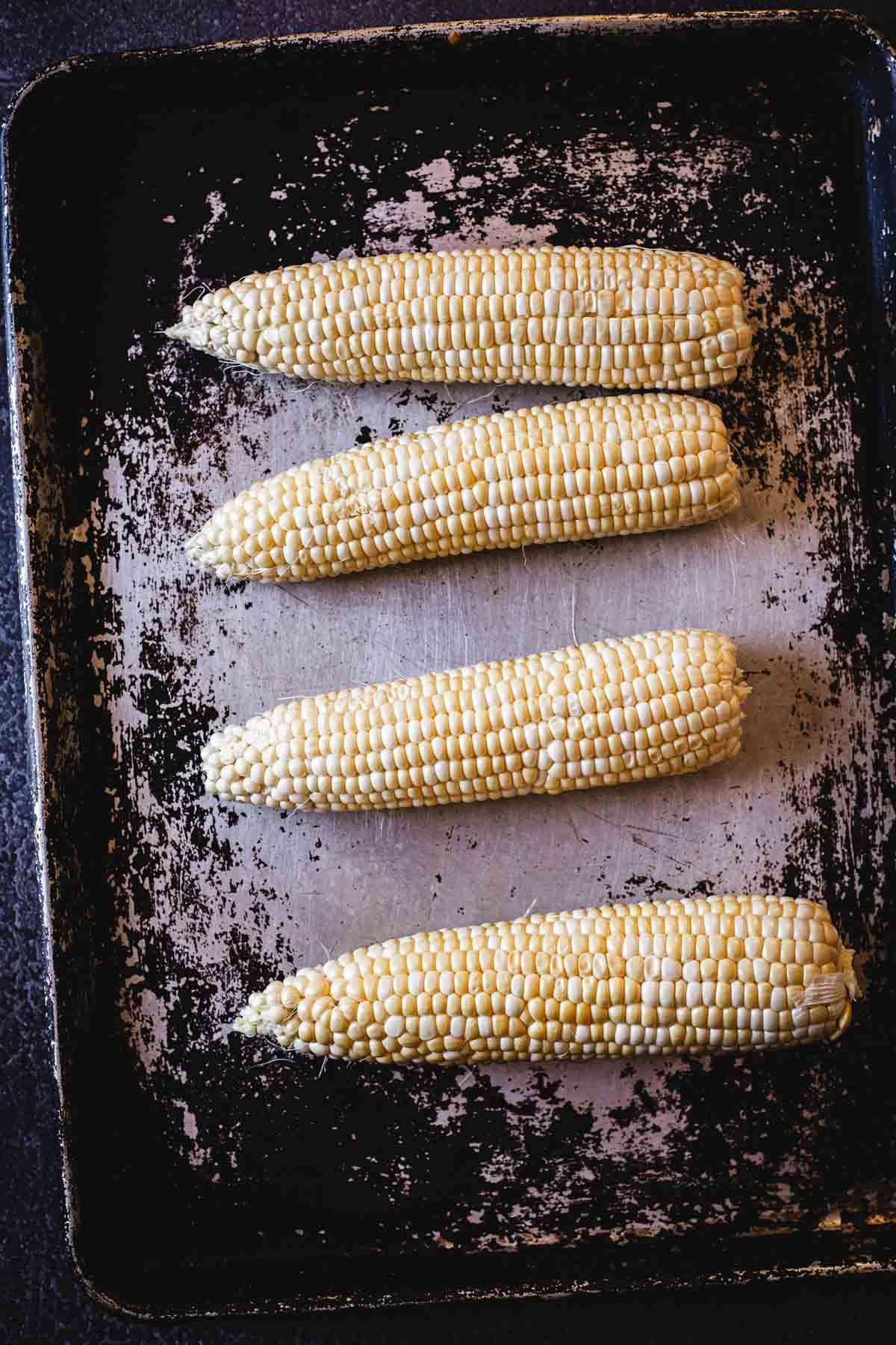 Corn on the cob on a baking sheet.