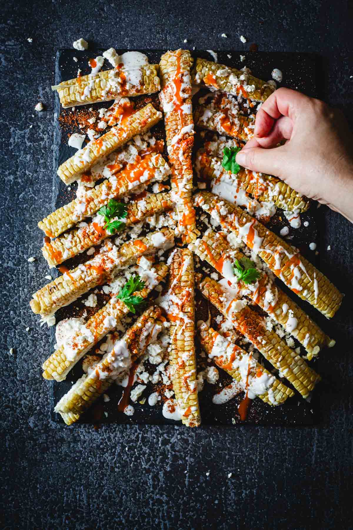 Corn on the cob with someone placing cilantro on top.