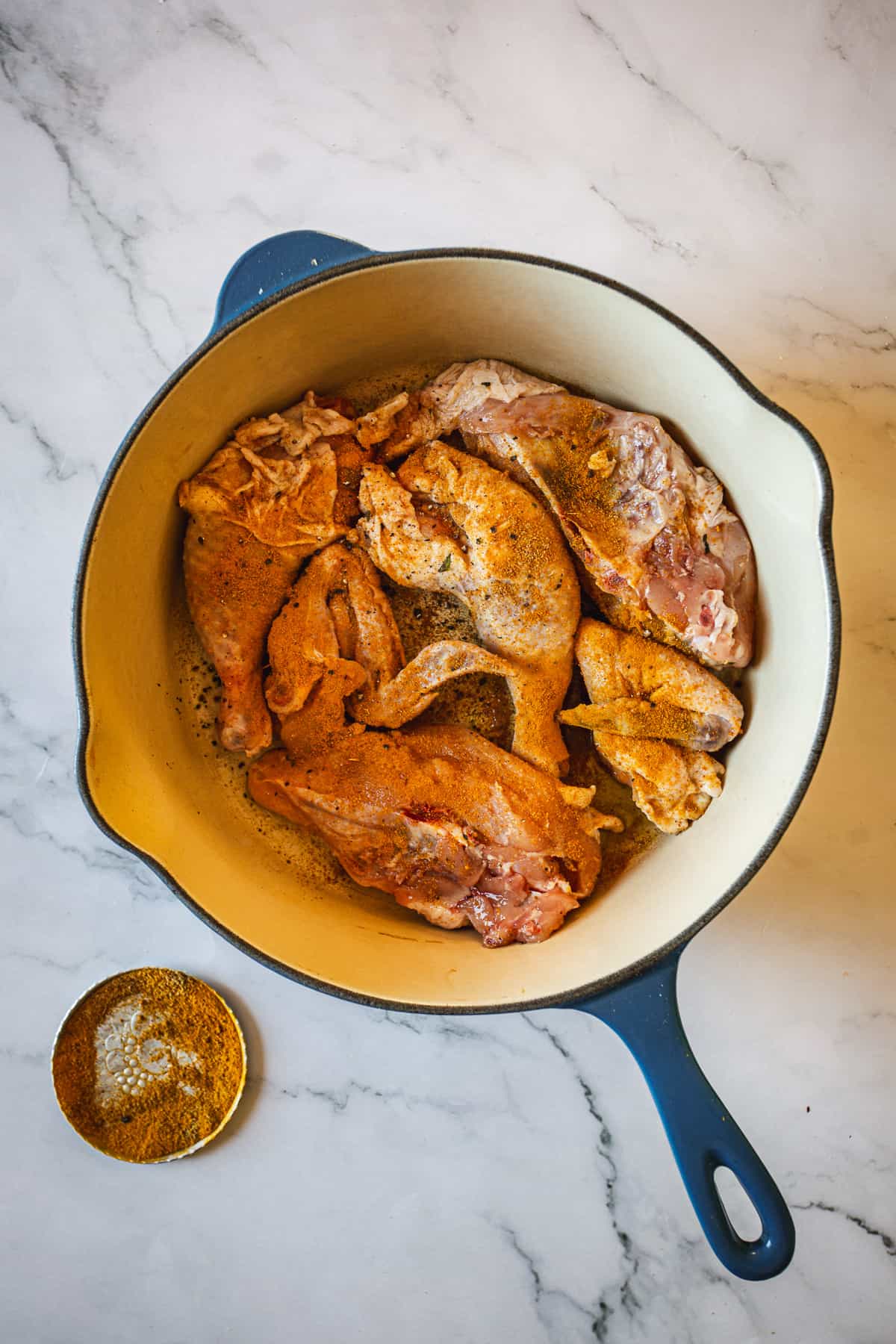 Chicken in a blue skillet on a marble countertop.