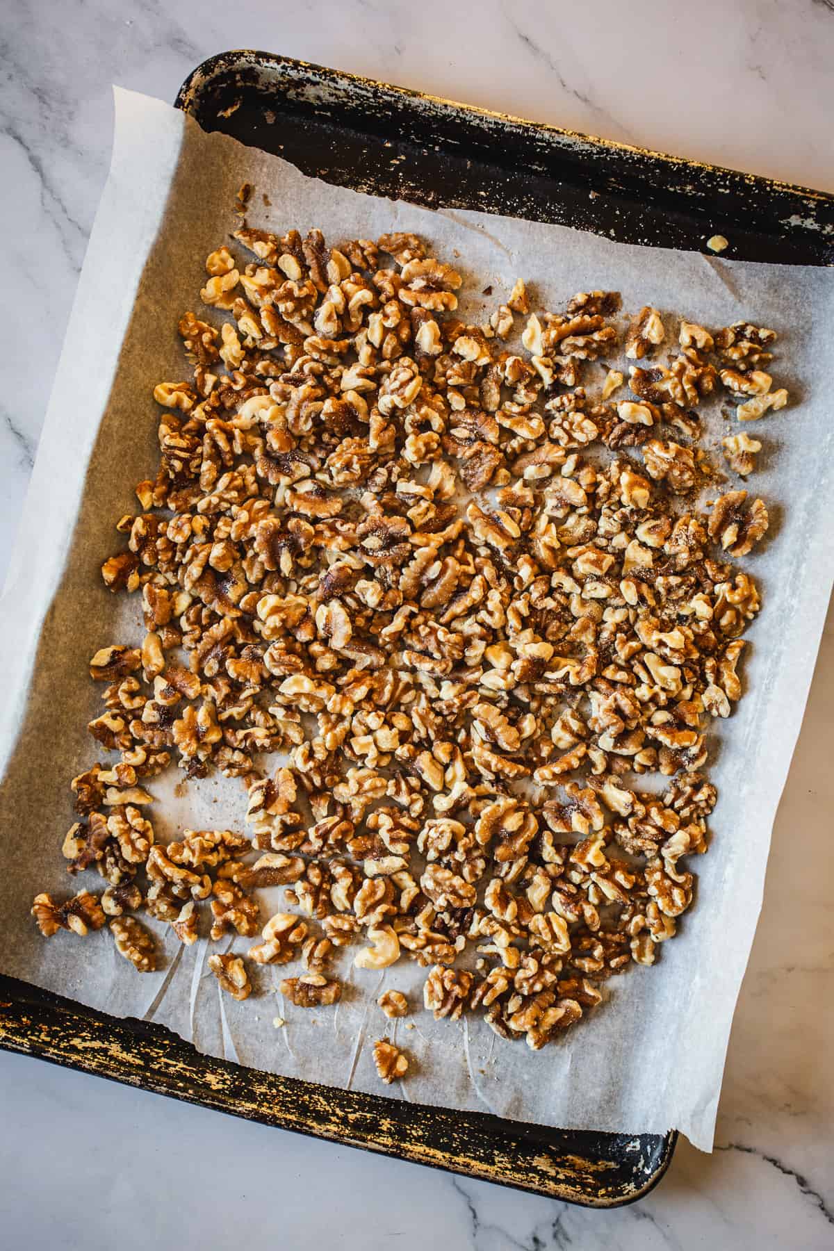 Walnuts on a baking sheet on a marble countertop.