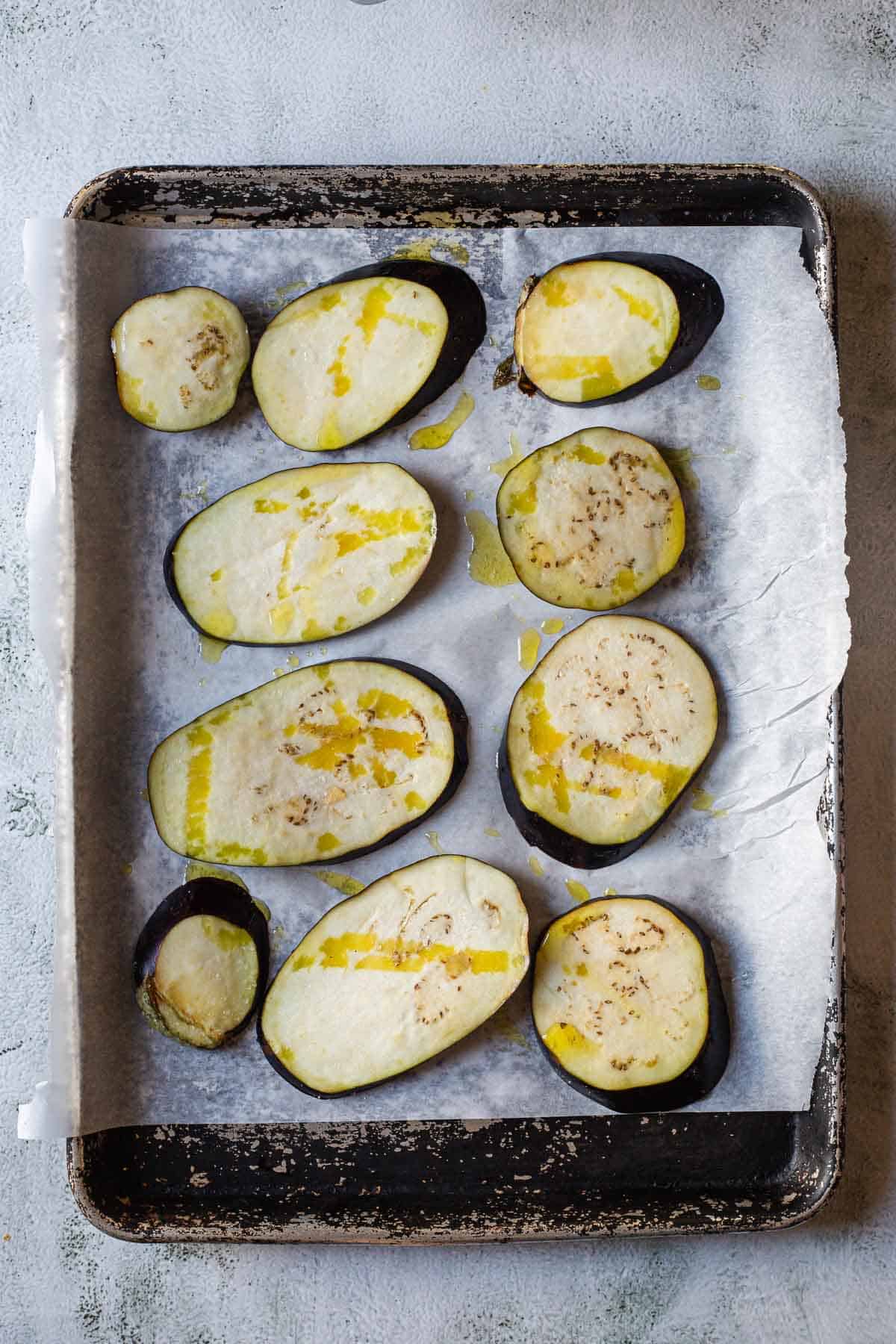 Sliced eggplants on a baking sheet with olive oil.