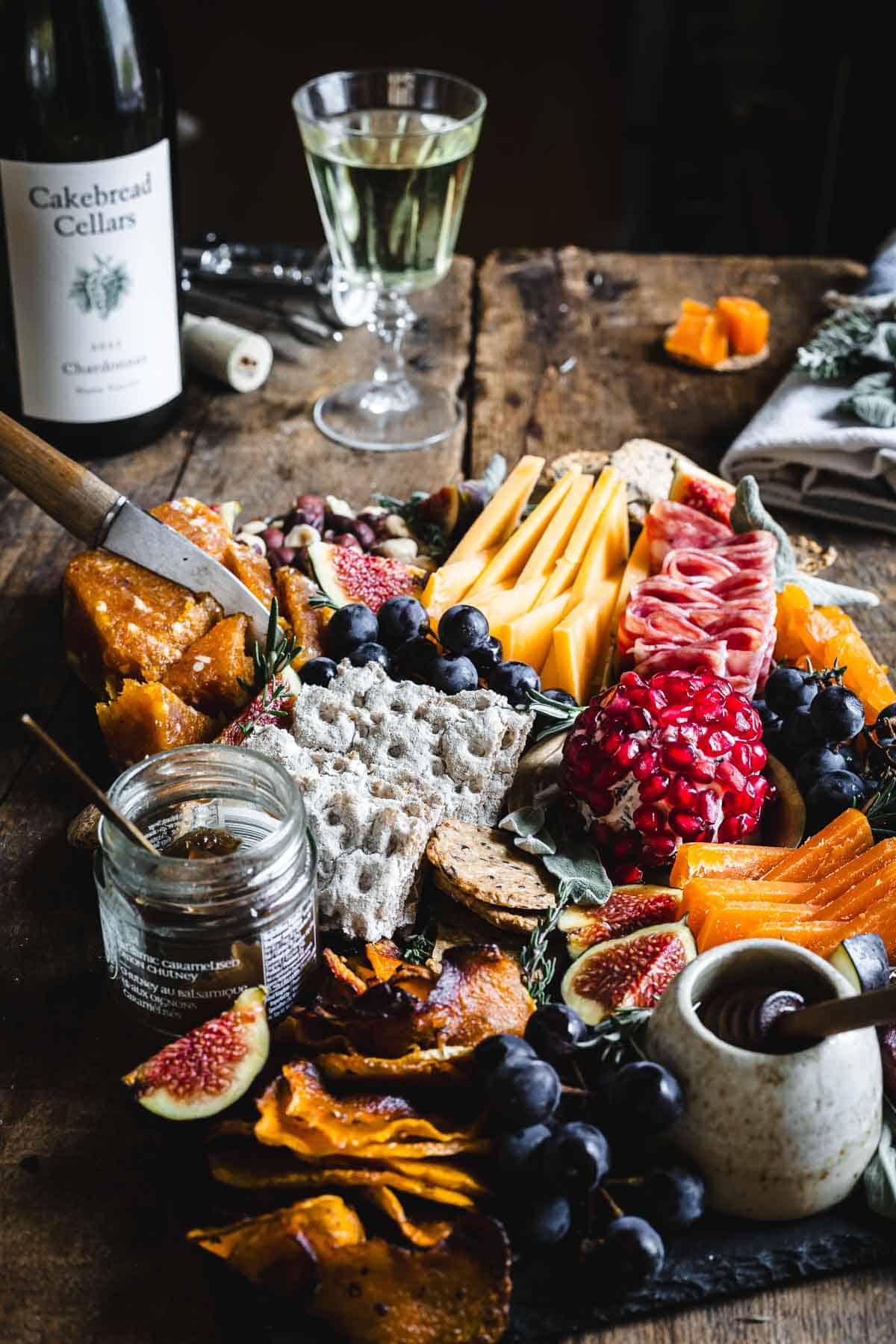 A platter of cheese and fruit with a bottle of wine.