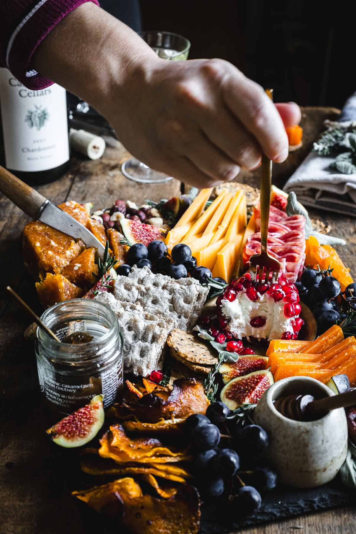 A person is dipping a knife into a platter of fruit and cheese.