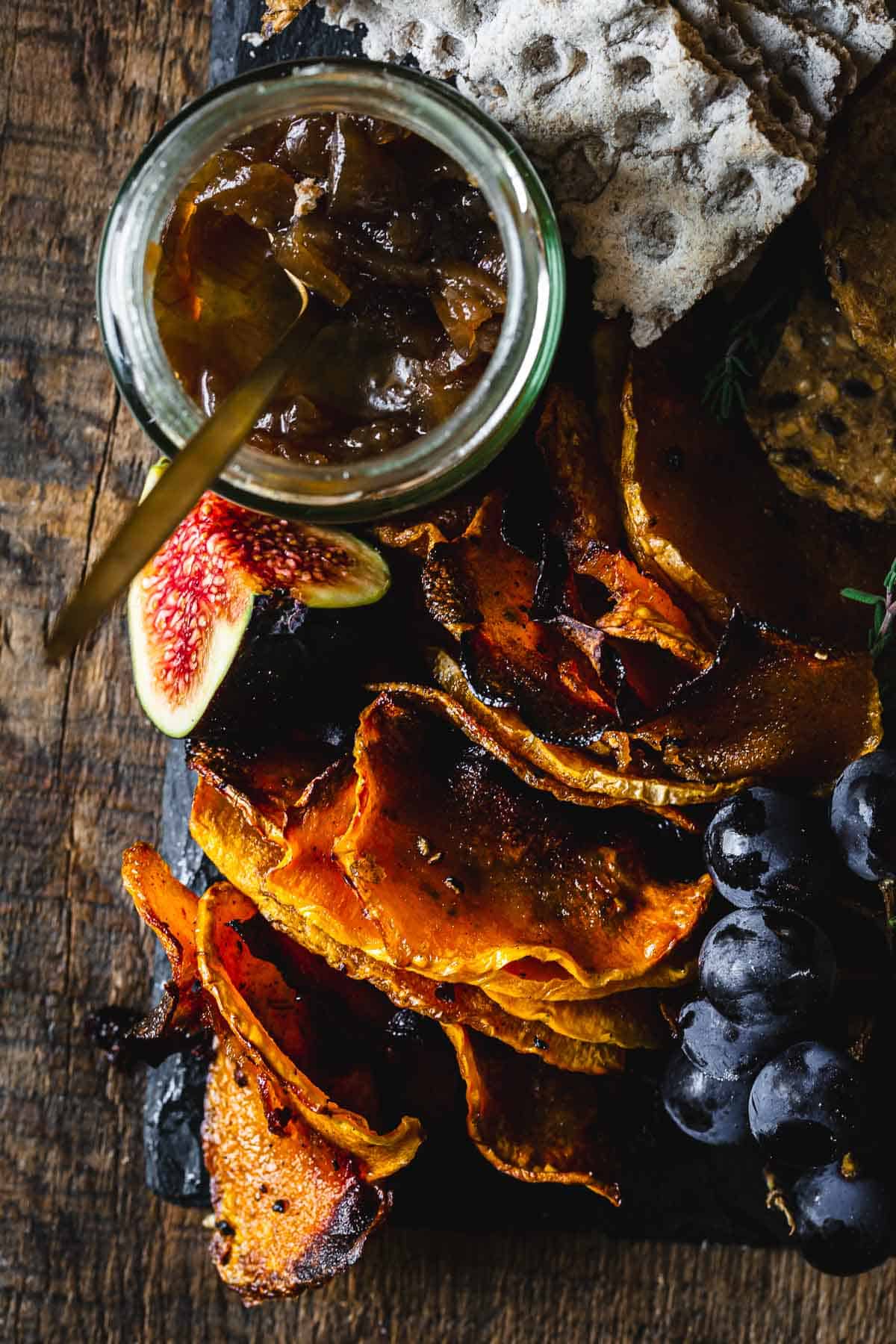 Sweet potato chips with figs and chutney on a wooden board.