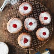 Donuts with powdered sugar and cherries on a cooling rack.