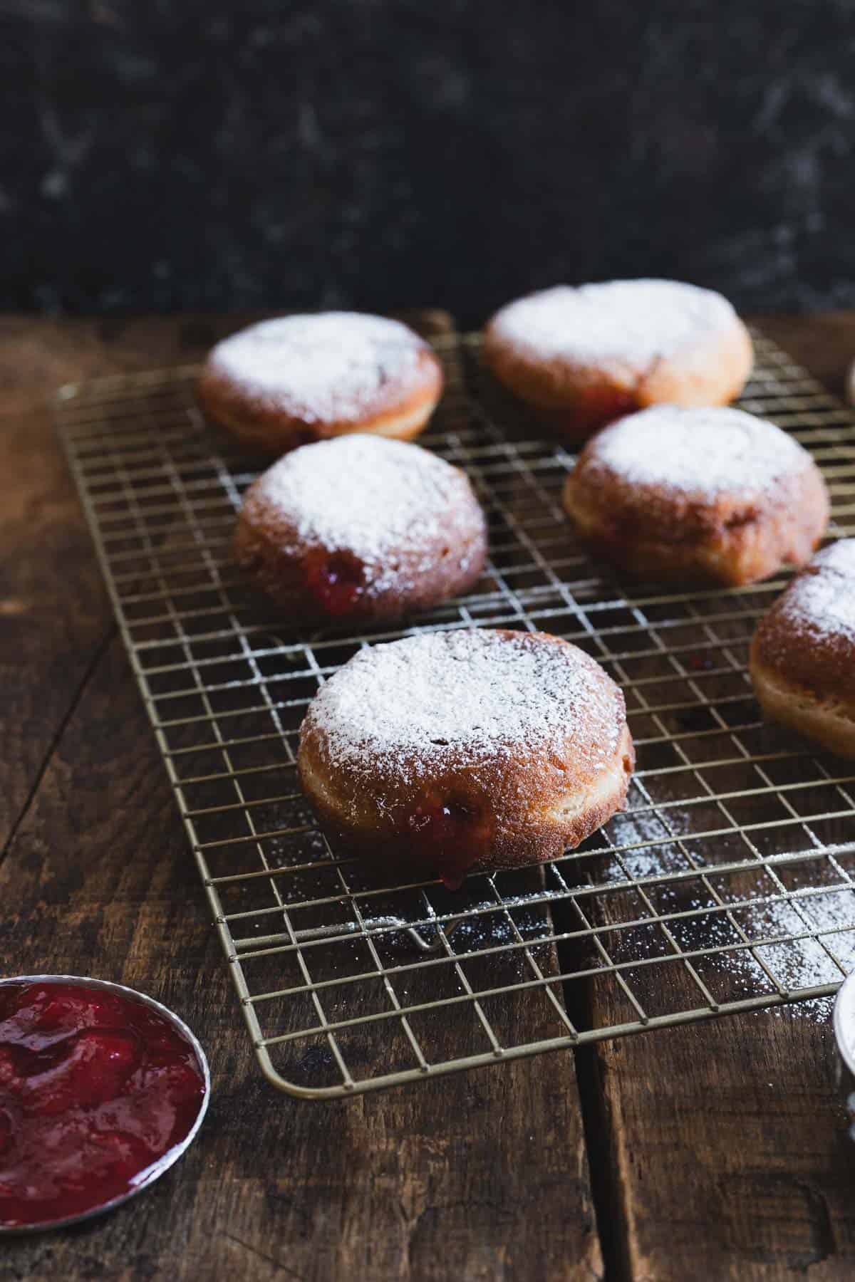 gluten free sufganiyot with jam and powdered sugar on a cooling rack.
