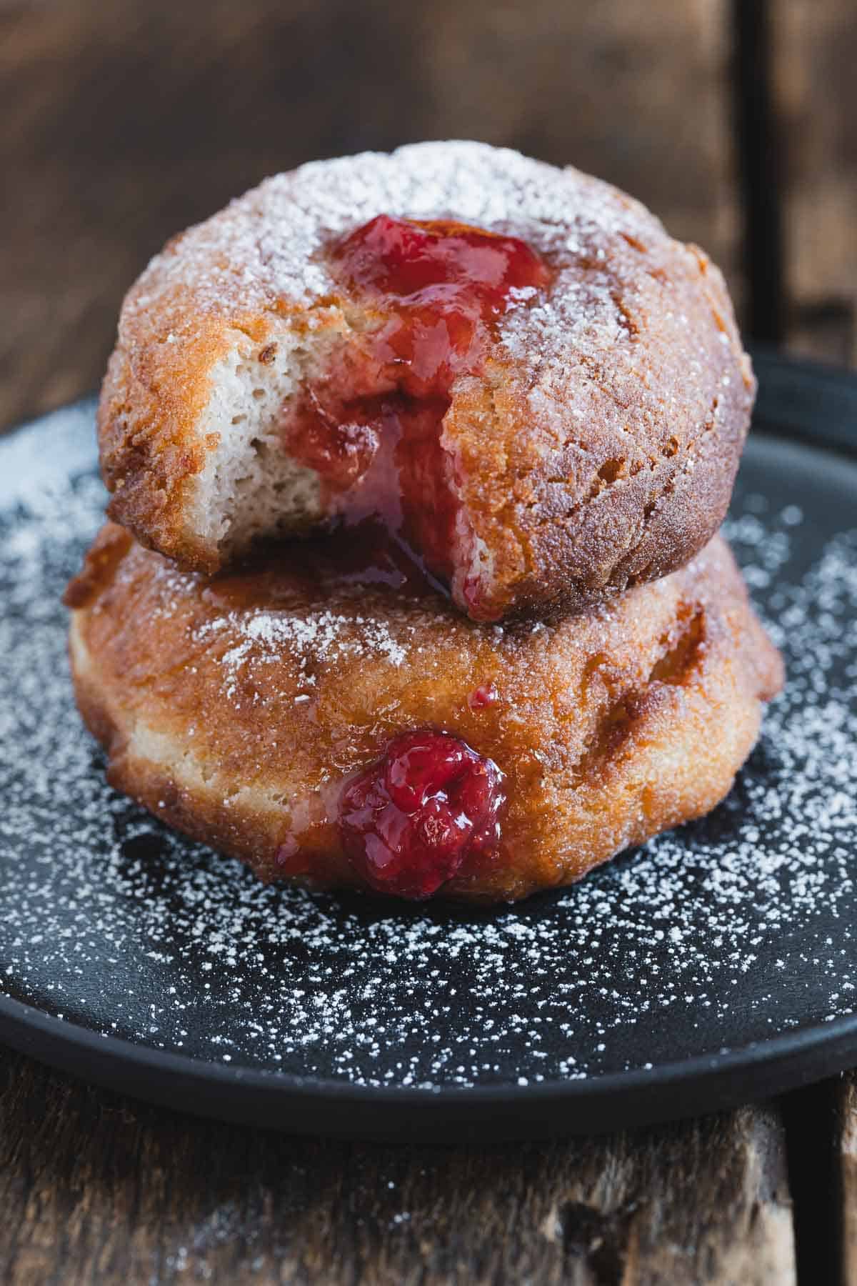 Donuts with raspberry jam and powdered sugar on a black plate.