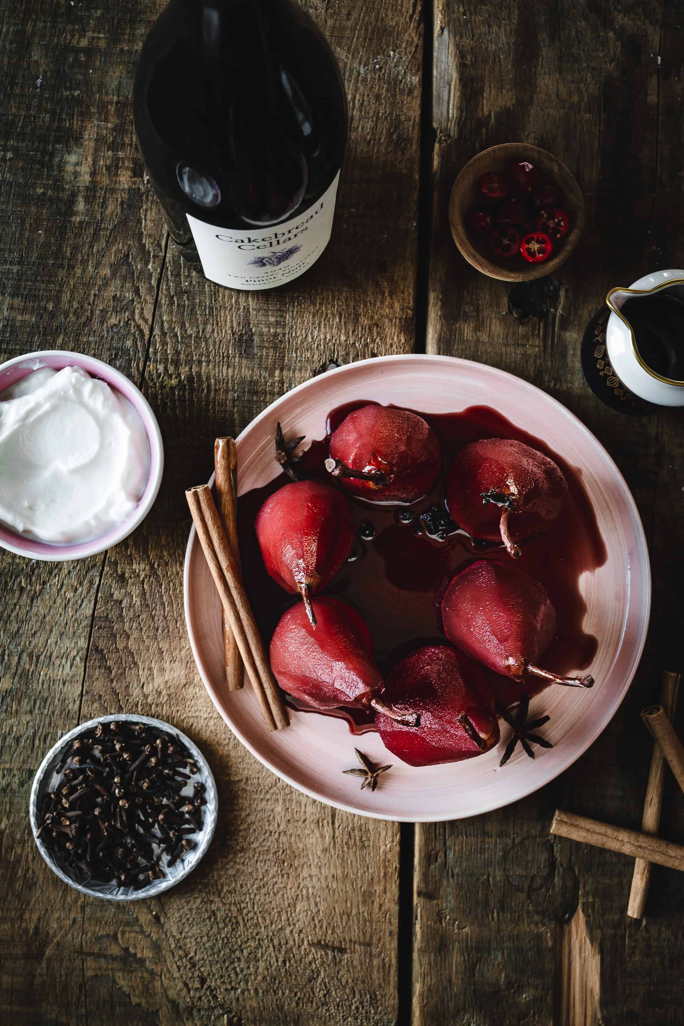 A plate with pears, cinnamon sticks and a bottle of wine.