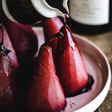 A person is pouring red wine on a plate of pears.