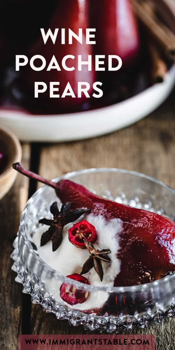 A glass dish of wine poached pears is placed on a wooden surface, topped with star anise and red berries, and set on a dollop of cream. The background features a blurred bowl with more wine poached pears. Text reads "Wine Poached Pears" and "www.immigrantstable.com".