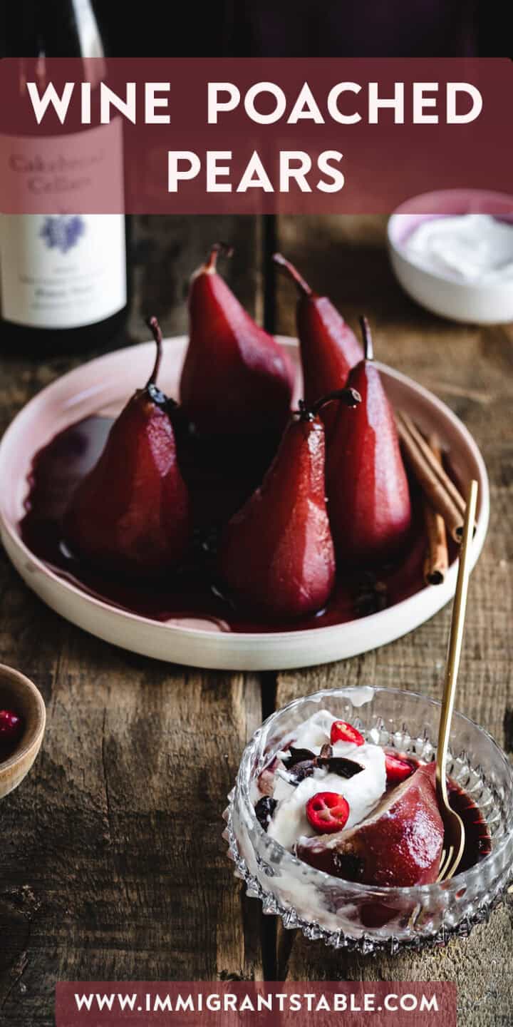 A wooden table set with a bowl containing four wine-poached pears, accompanied by cinnamon sticks and berries. A glass bowl in the foreground showcases a wine-poached pear with whipped cream and pomegranate seeds. A bottle of wine and a bowl of whipped cream are in the background. "WINE POACHED PEARS" text is displayed at the top, with "www.immigrantstable.com