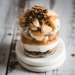 A yogurt parfait with apples and granola on a white plate.