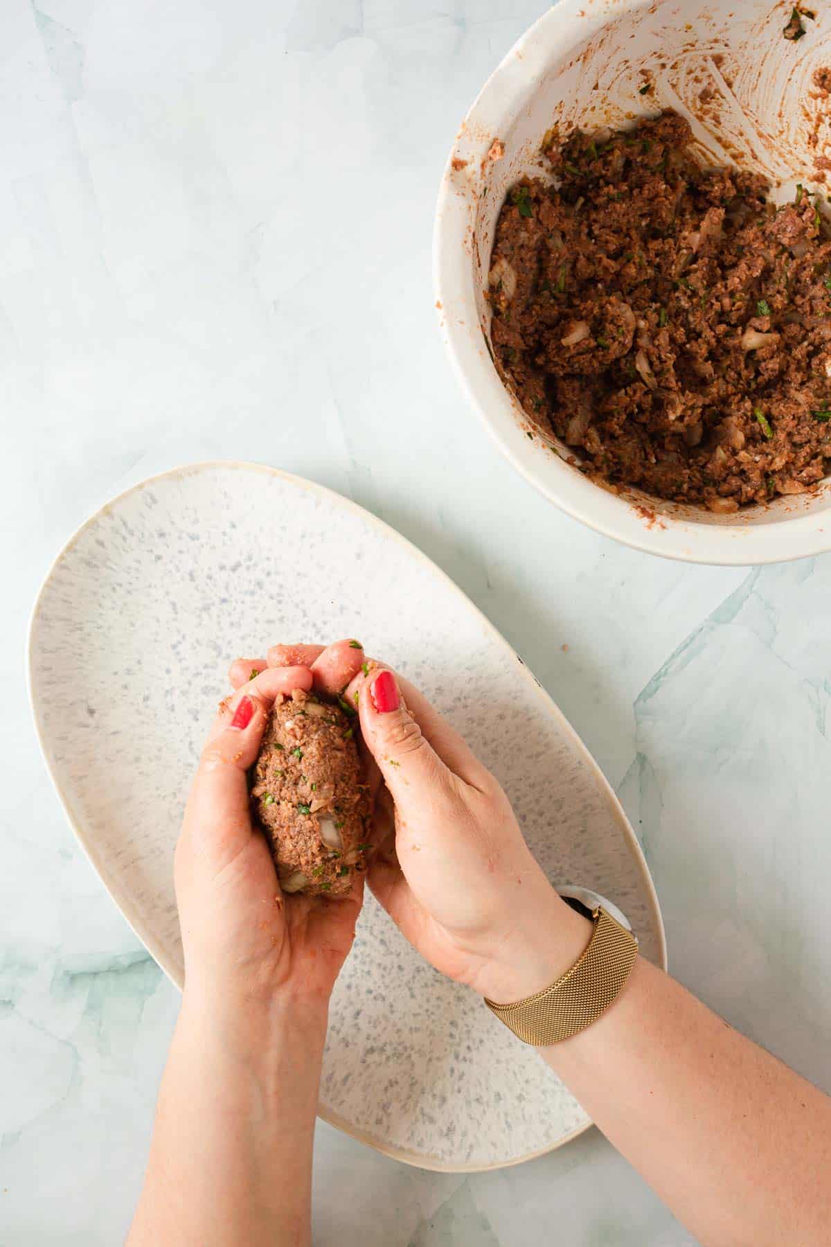 A person putting kofta kebabs on a plate.