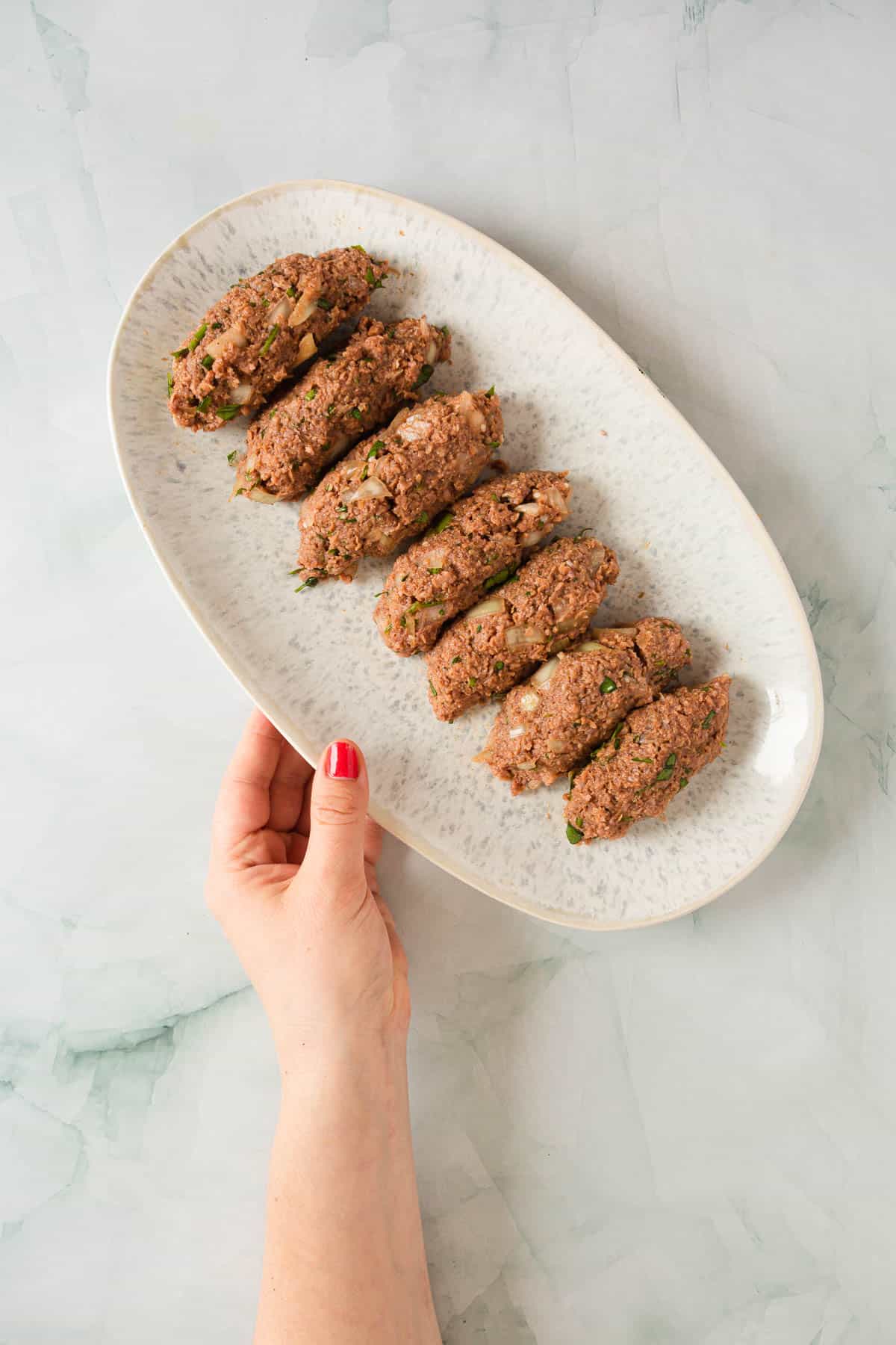 A person holding a plate of kofta kebabs.