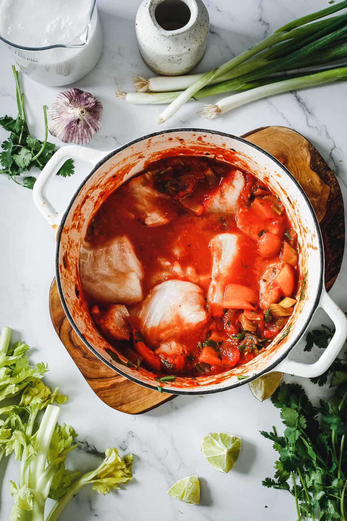 A pot of stew with vegetables and herbs on a table.